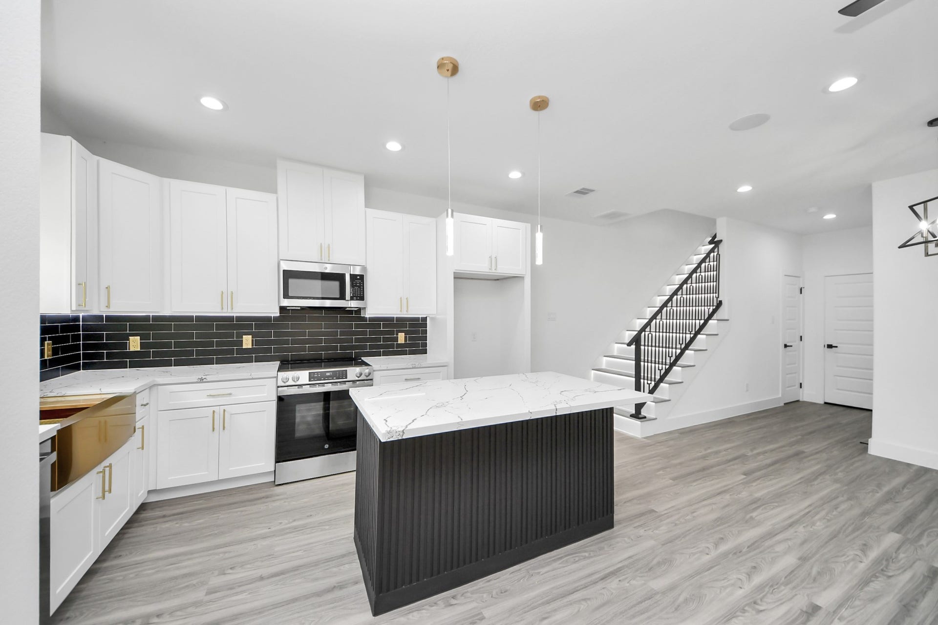 6711 Crestmont Street, Houston, TX 77033 Sleek modern kitchen with white cabinetry, marble countertops, and a stylish black tile backsplash. The open layout flows seamlessly into the living area, accented by elegant pendant lighting and a contemporary staircase.