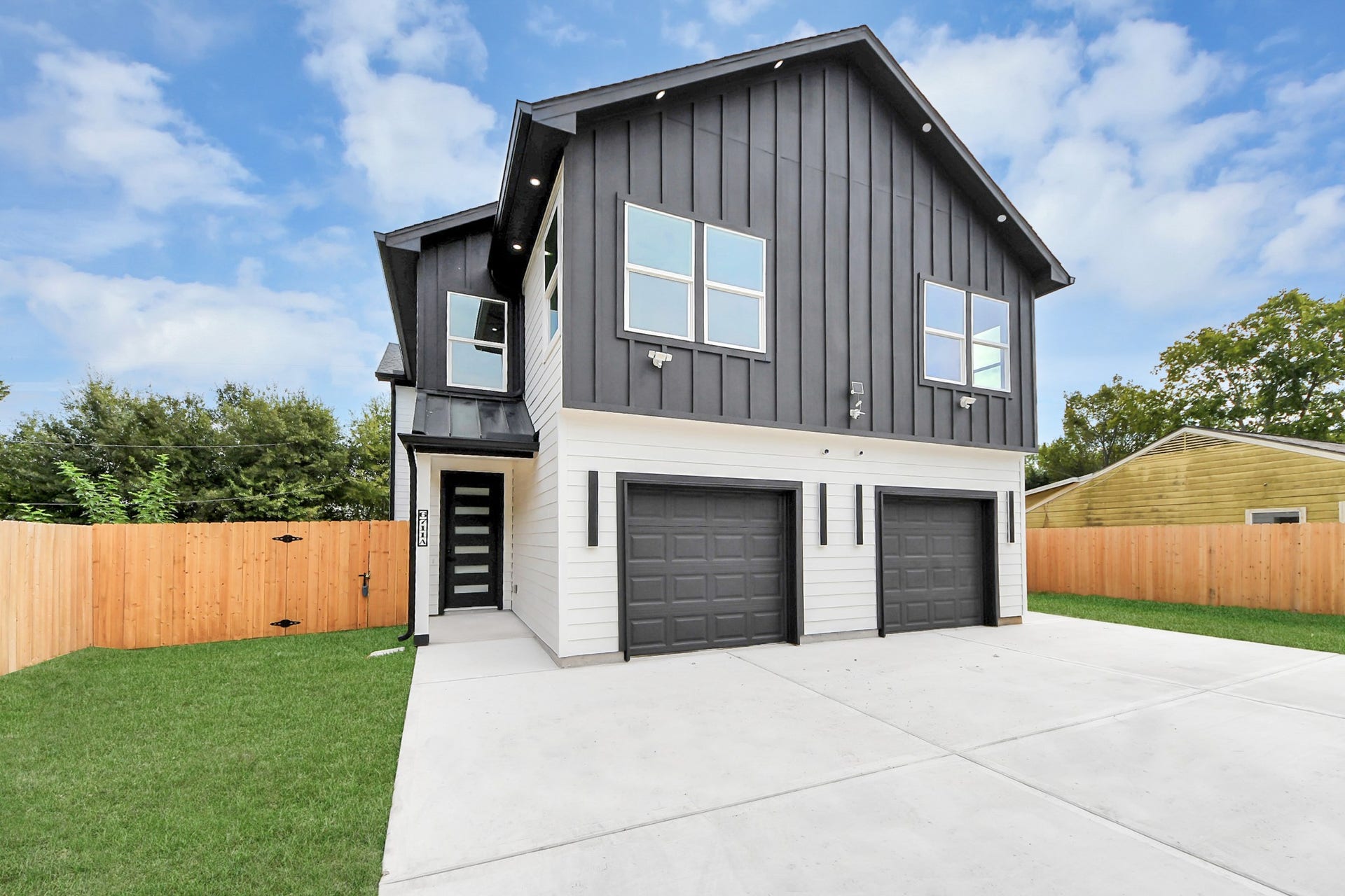 6711 Crestmont Street, Houston, TX 77033 Modern duplex featuring a sleek black facade with two single-car garages, set on a spacious driveway and surrounded by a wooden privacy fence.