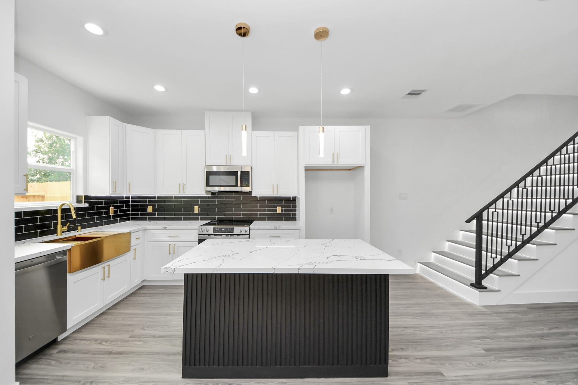 6711 Crestmont Street, Houston, TX 77033 Sleek modern kitchen featuring a large island with marble countertops, gold accents, and stylish black tile backsplash, complemented by elegant pendant lighting and adjacent to a contemporary staircase.