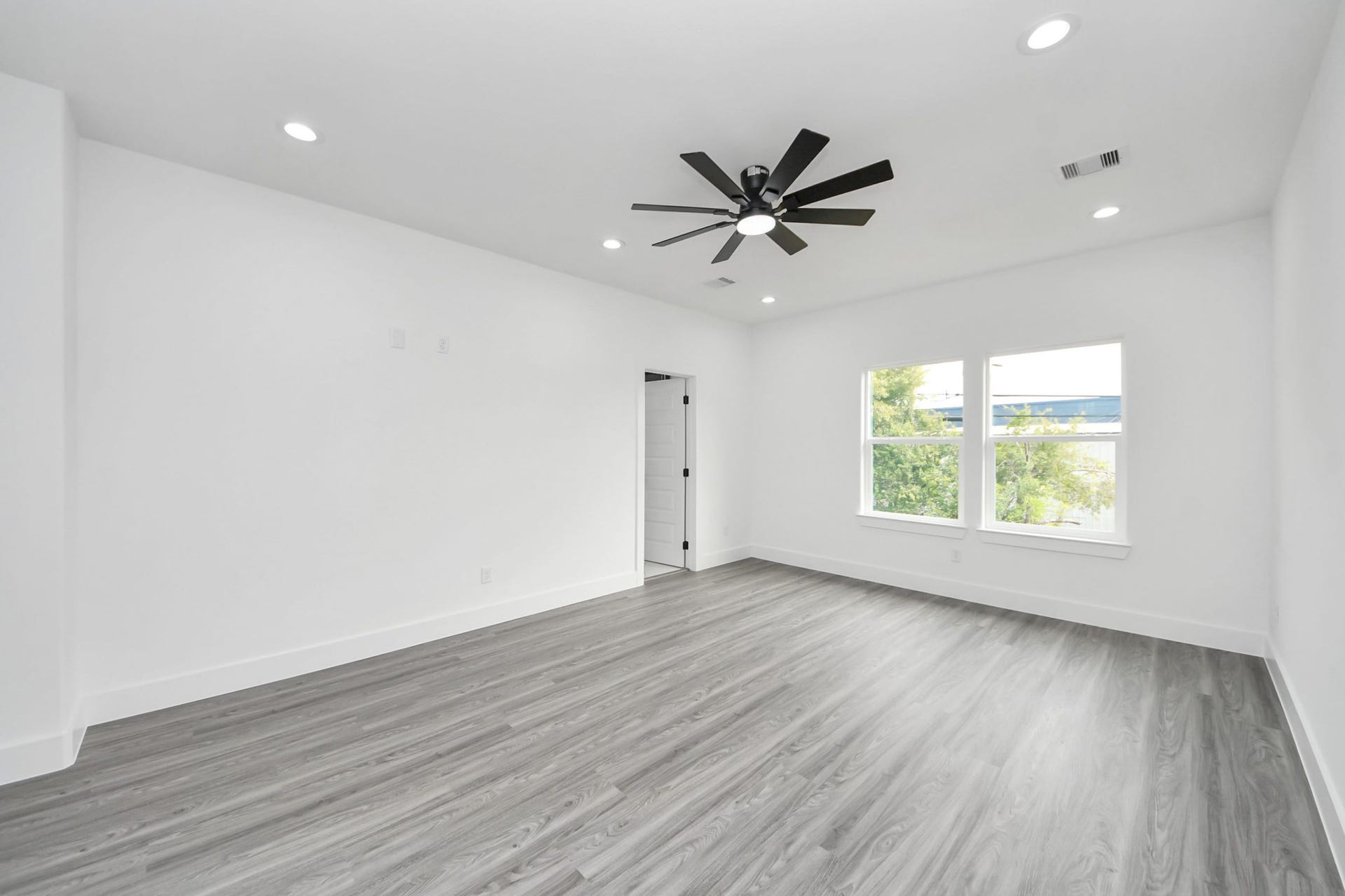 6711 Crestmont Street, Houston, TX 77033 Spacious, bright room with modern wood flooring, recessed lighting, and a sleek ceiling fan, offering ample natural light through large windows.