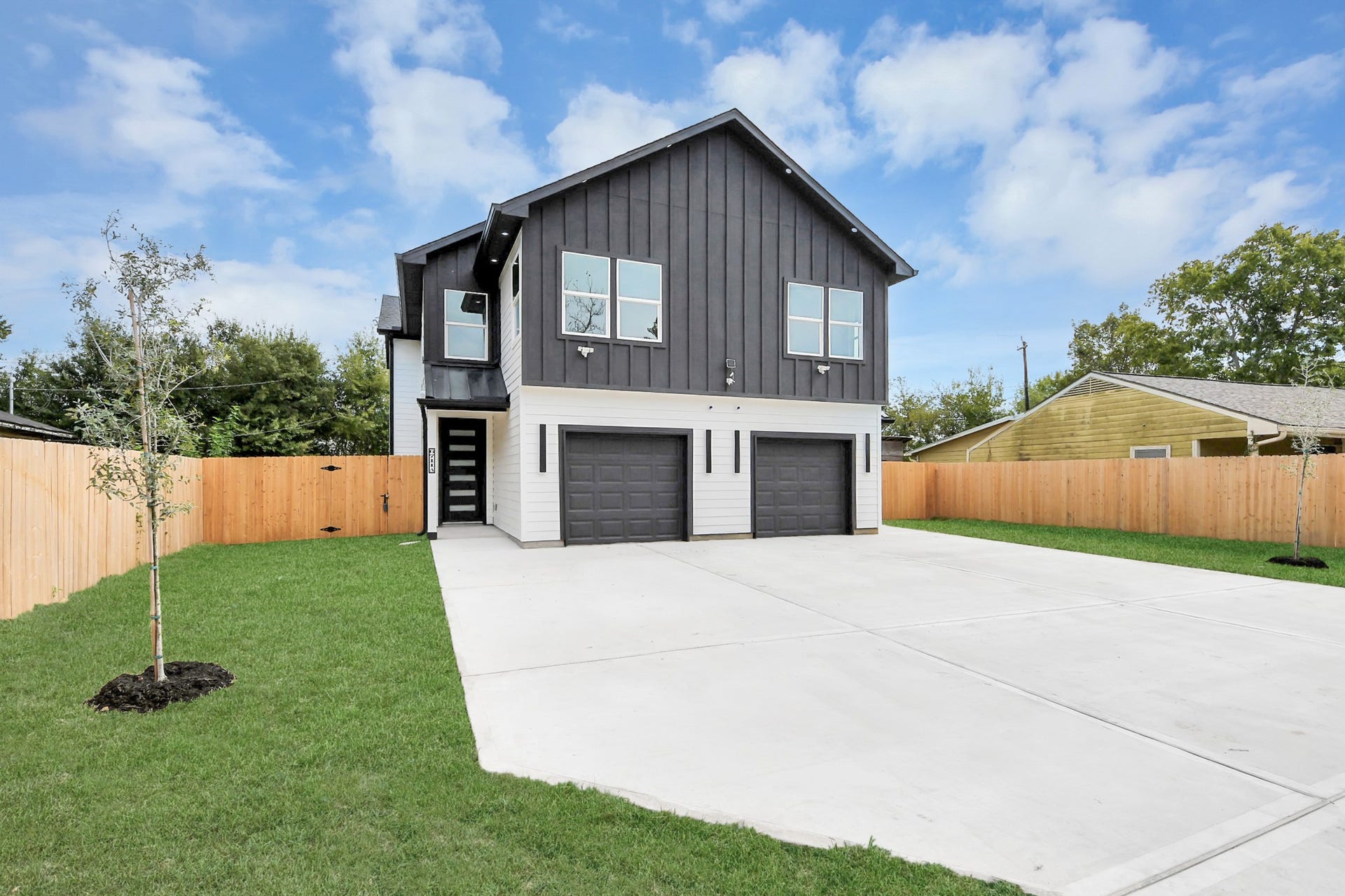 6711 Crestmont Street, Houston, TX 77033 Modern two-story home with sleek dark siding, dual garage doors, and a spacious driveway, set within a neatly fenced yard.