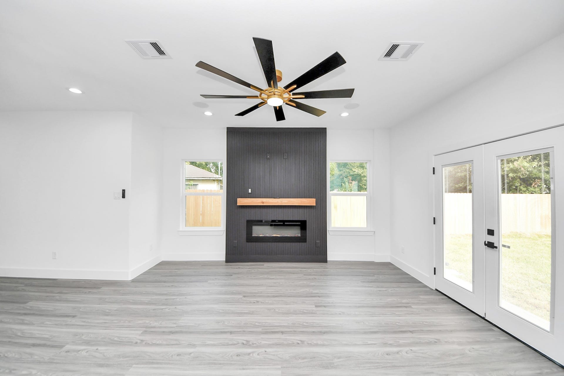 6711 Crestmont Street, Houston, TX 77033 Bright and modern living room featuring sleek wood flooring, a striking black accent wall with a contemporary fireplace, and elegant French doors opening to the backyard.
