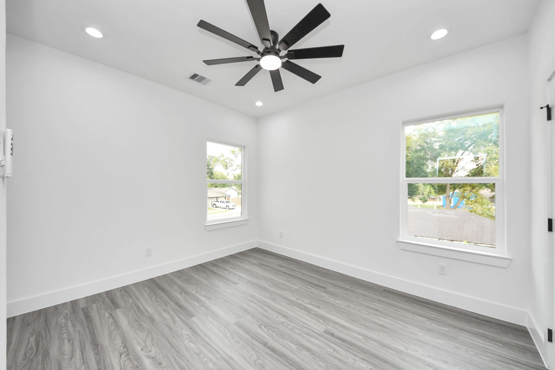 6711 Crestmont Street, Houston, TX 77033 Bright and airy room featuring sleek gray flooring, modern recessed lighting, and a stylish ceiling fan, highlighted by ample natural light from two large windows.