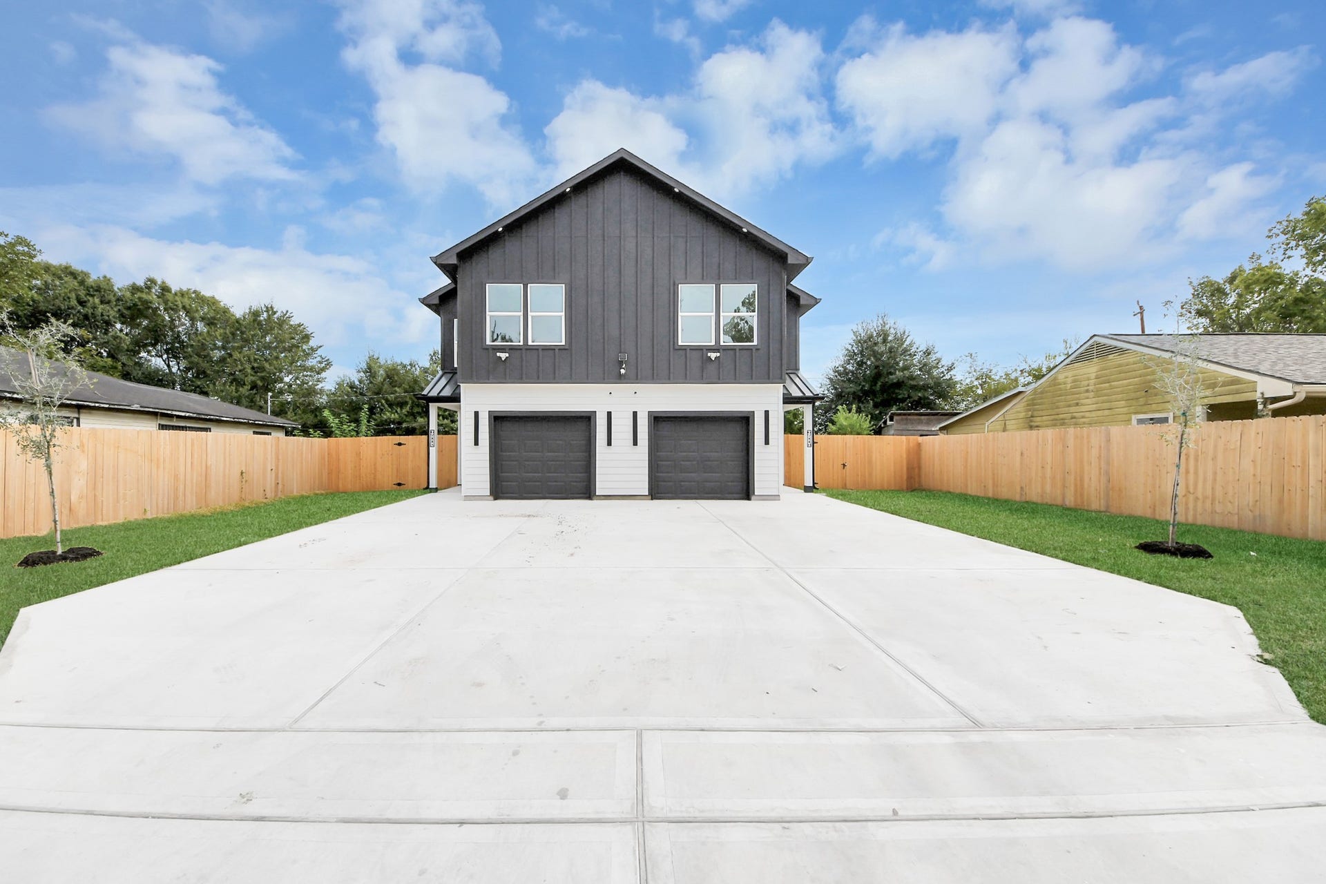 6711 Crestmont Street, Houston, TX 77033 Modern two-story home with a striking dark facade, featuring dual garages and a spacious concrete driveway. The property is surrounded by a wooden privacy fence and landscaped with fresh greenery, offering a blend of style and functionality.