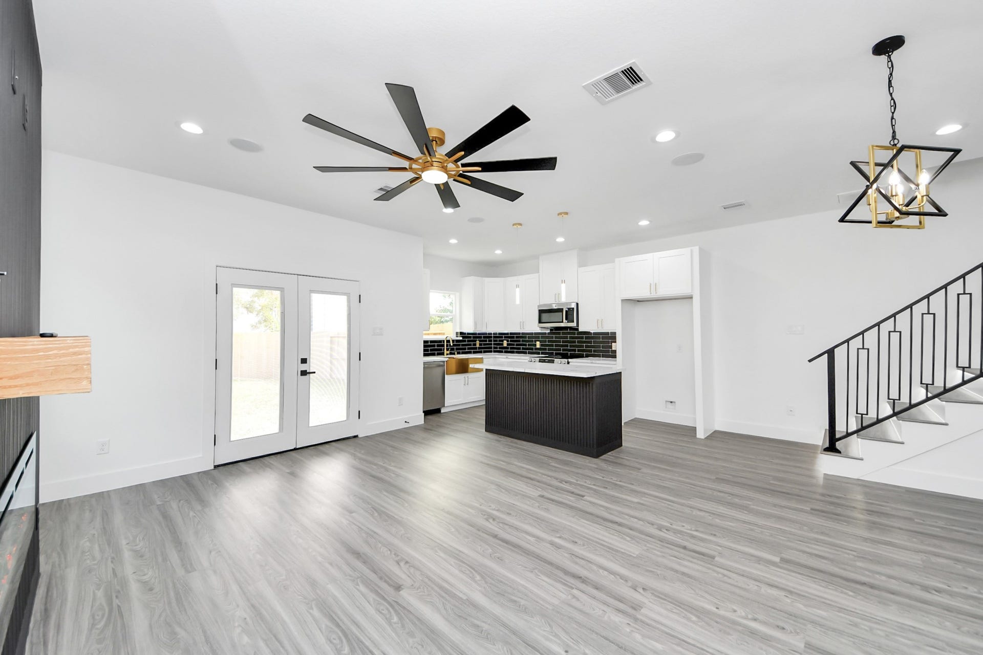 6711 Crestmont Street, Houston, TX 77033 Spacious open-concept living area featuring sleek flooring, a modern kitchen with black subway tile backsplash, and stylish lighting fixtures, complemented by French doors leading to the backyard.
