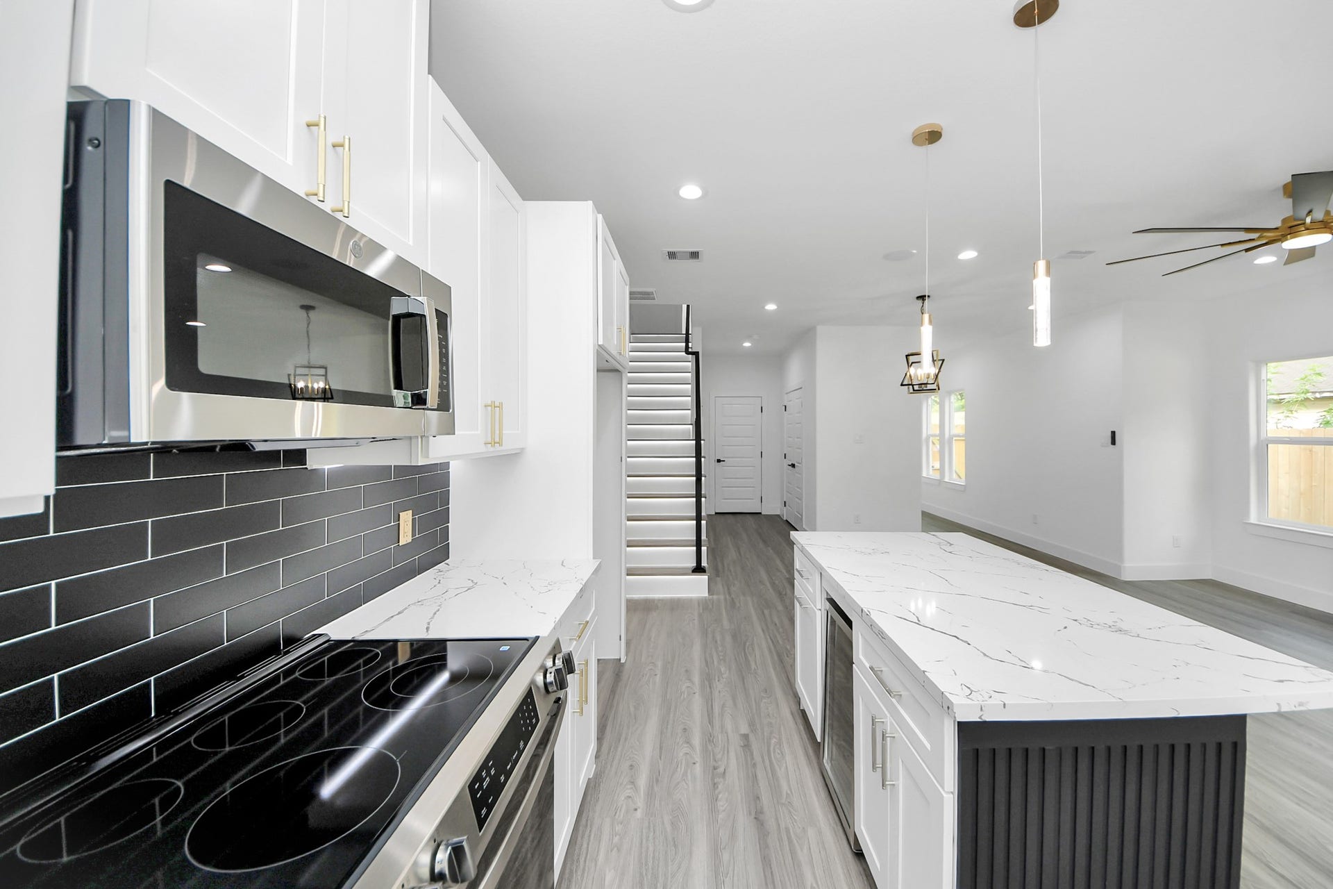 6711 Crestmont Street, Houston, TX 77033 Sleek modern kitchen with a stylish black subway tile backsplash, stainless steel appliances, and a spacious marble island. Open-concept layout with elegant lighting and a contemporary staircase.