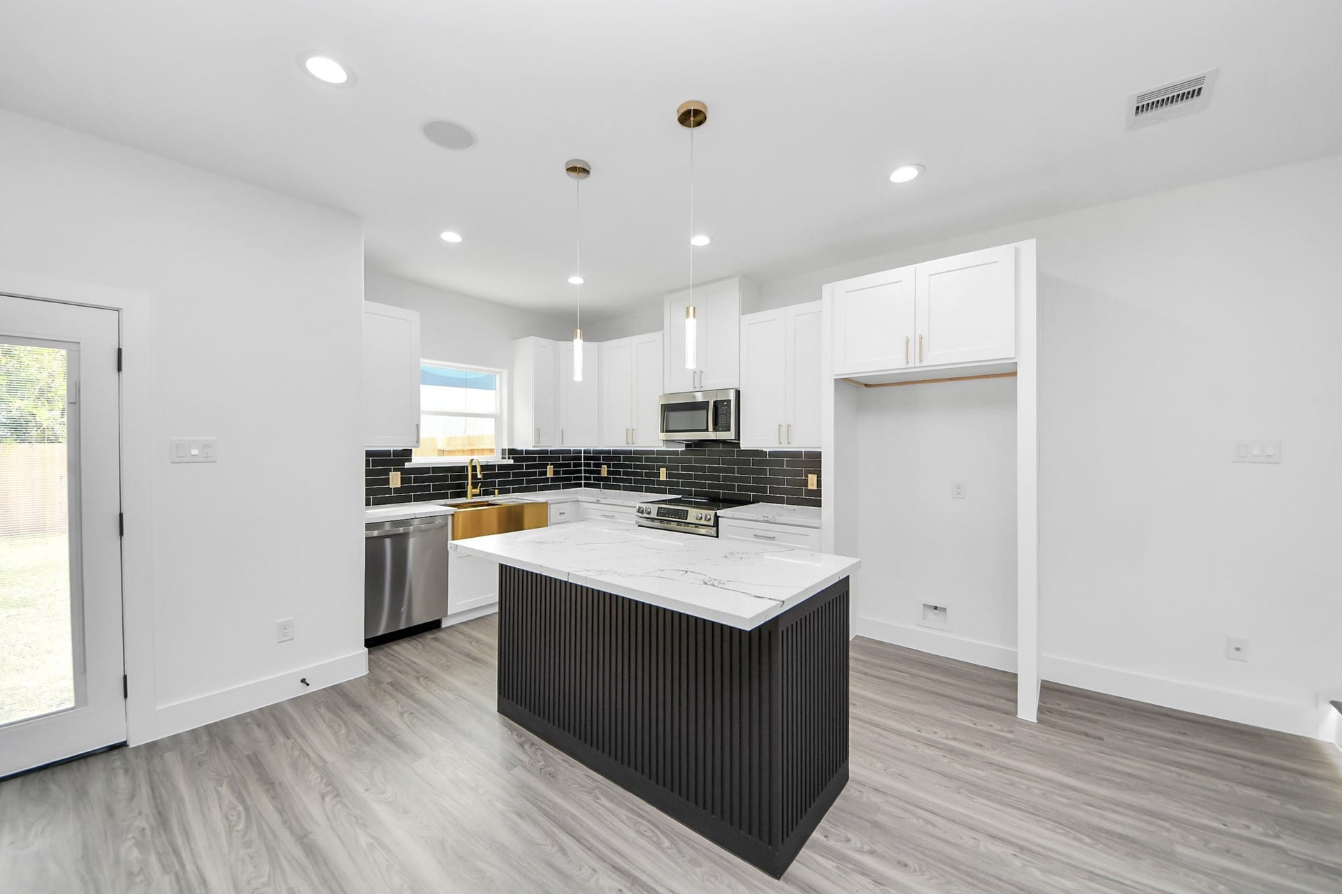 6711 Crestmont Street, Houston, TX 77033 Sleek modern kitchen featuring a stylish black island with marble countertop, stainless steel appliances, and elegant black subway tile backsplash.