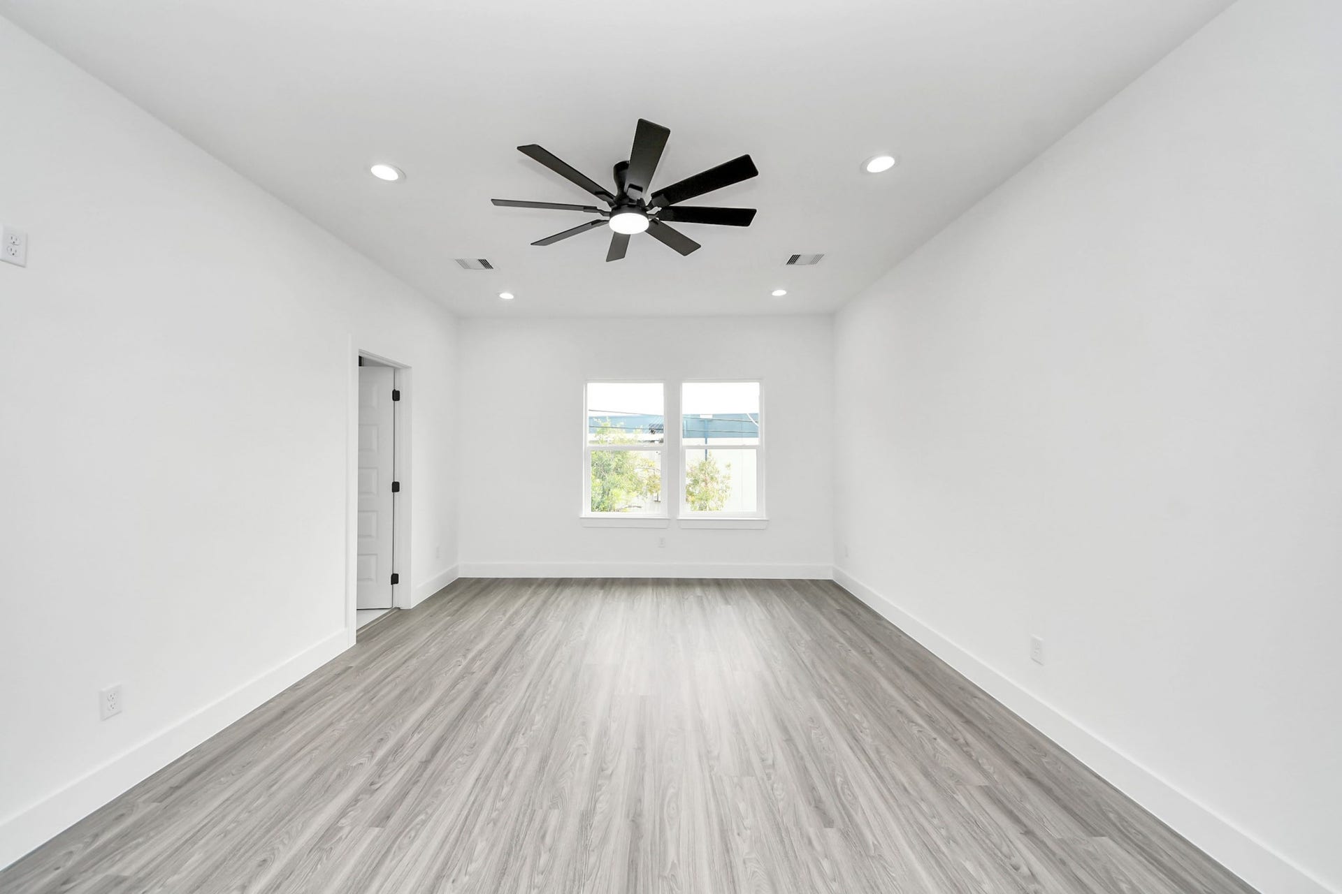 6711 Crestmont Street, Houston, TX 77033 Spacious room with sleek wood flooring, fresh white walls, and a modern ceiling fan, offering ample natural light through a large window.