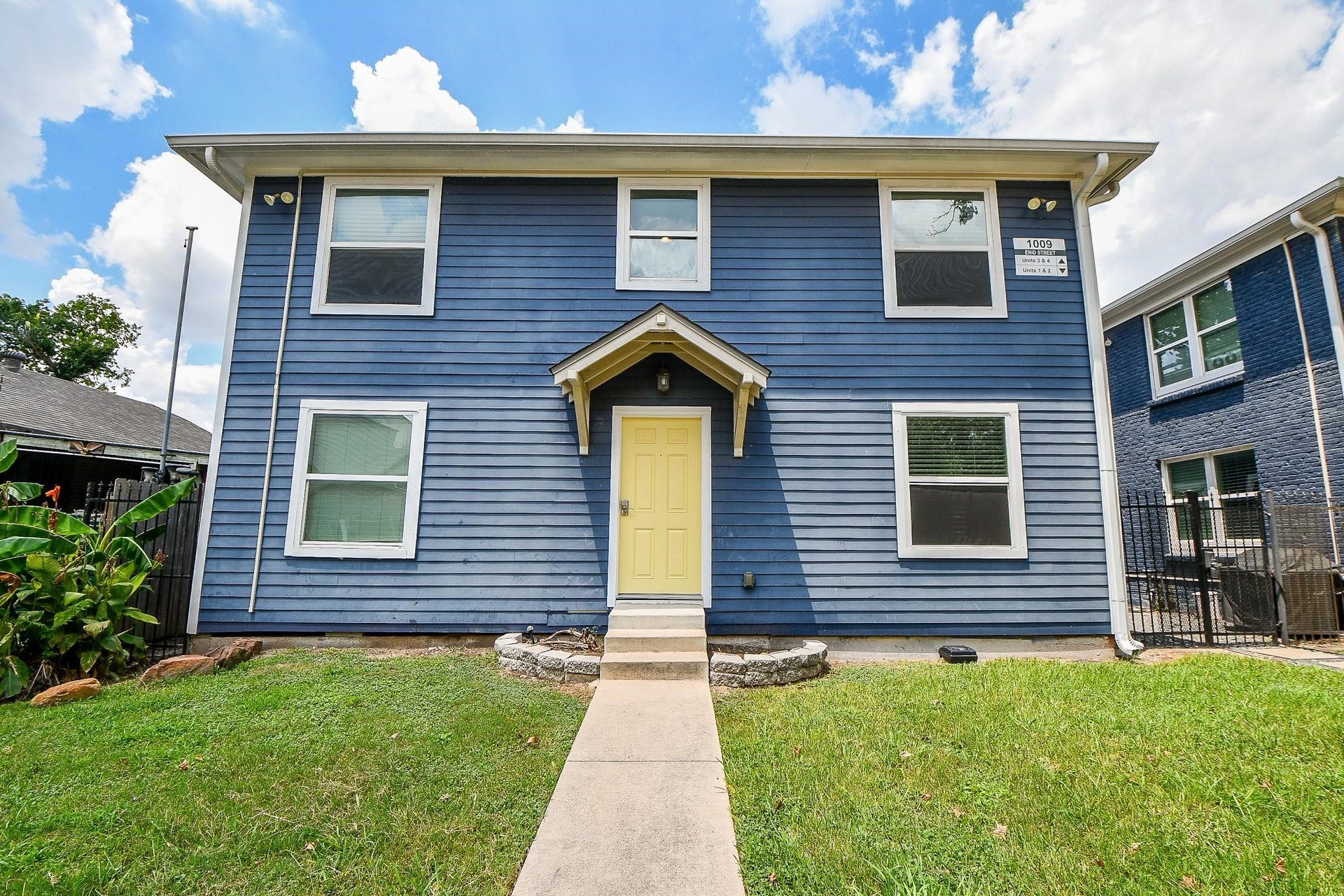 Stylish four-unit home with a statement yellow door, clean-cut lawn, and easy front access.