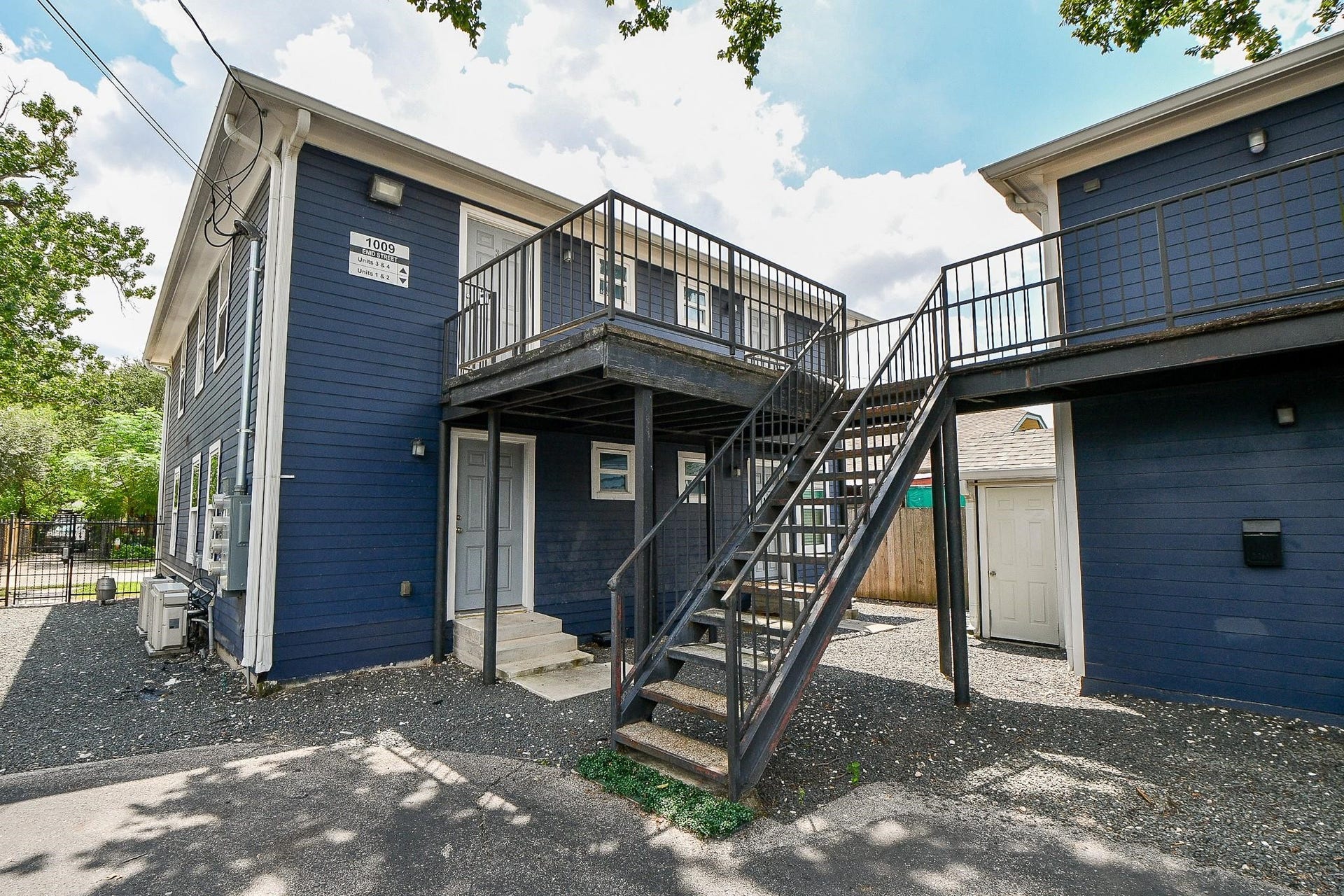 Staircase leads to the second-floor entrance, with gravel-covered ground for low-maintenance landscaping.