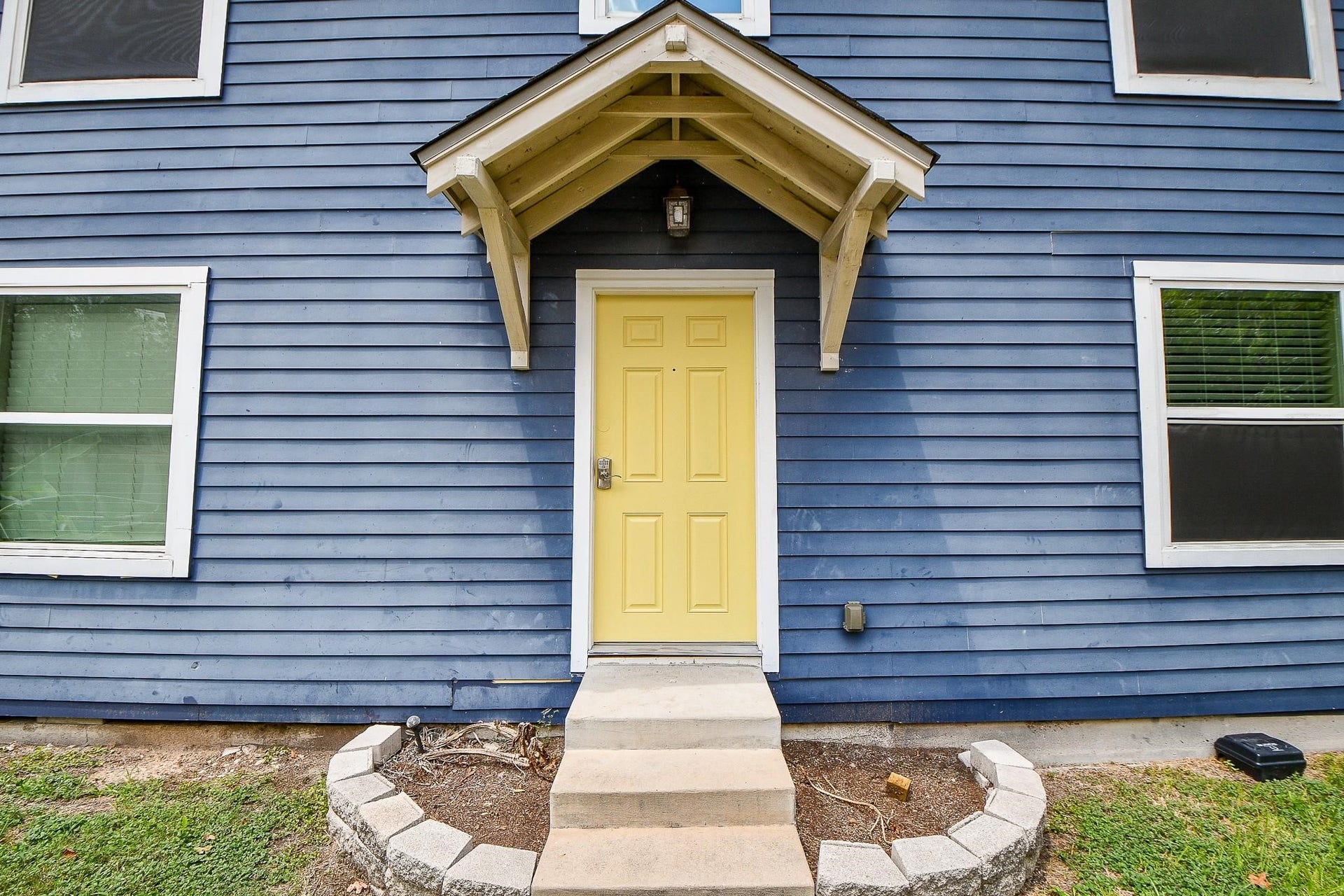 Charming front entrance with a cheerful yellow door and small overhang, set against classic blue siding. Simple landscaping frames the steps, adding curb appeal.
