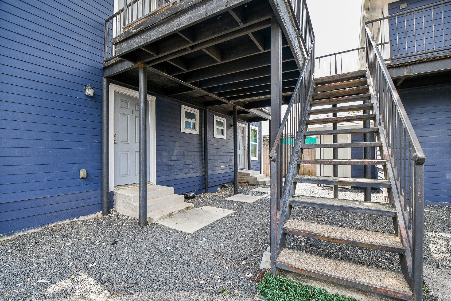Staircase leads to the second-floor entrance, with gravel-covered ground for low-maintenance landscaping.