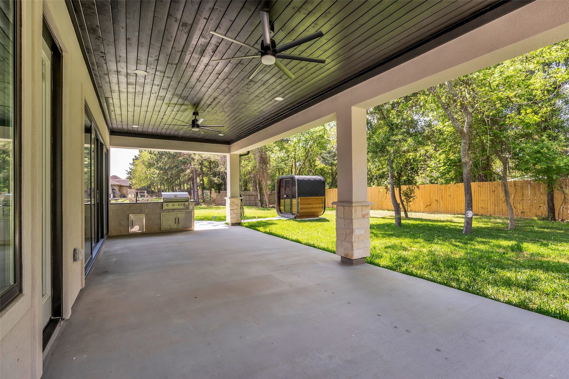 22420 Meadowhurst Circle W, Tomball, TX 77377 This spacious covered patio features a ceiling with fans, an outdoor kitchen area with a built-in grill, and overlooks a lush, fenced backyard, perfect for entertaining and relaxation.