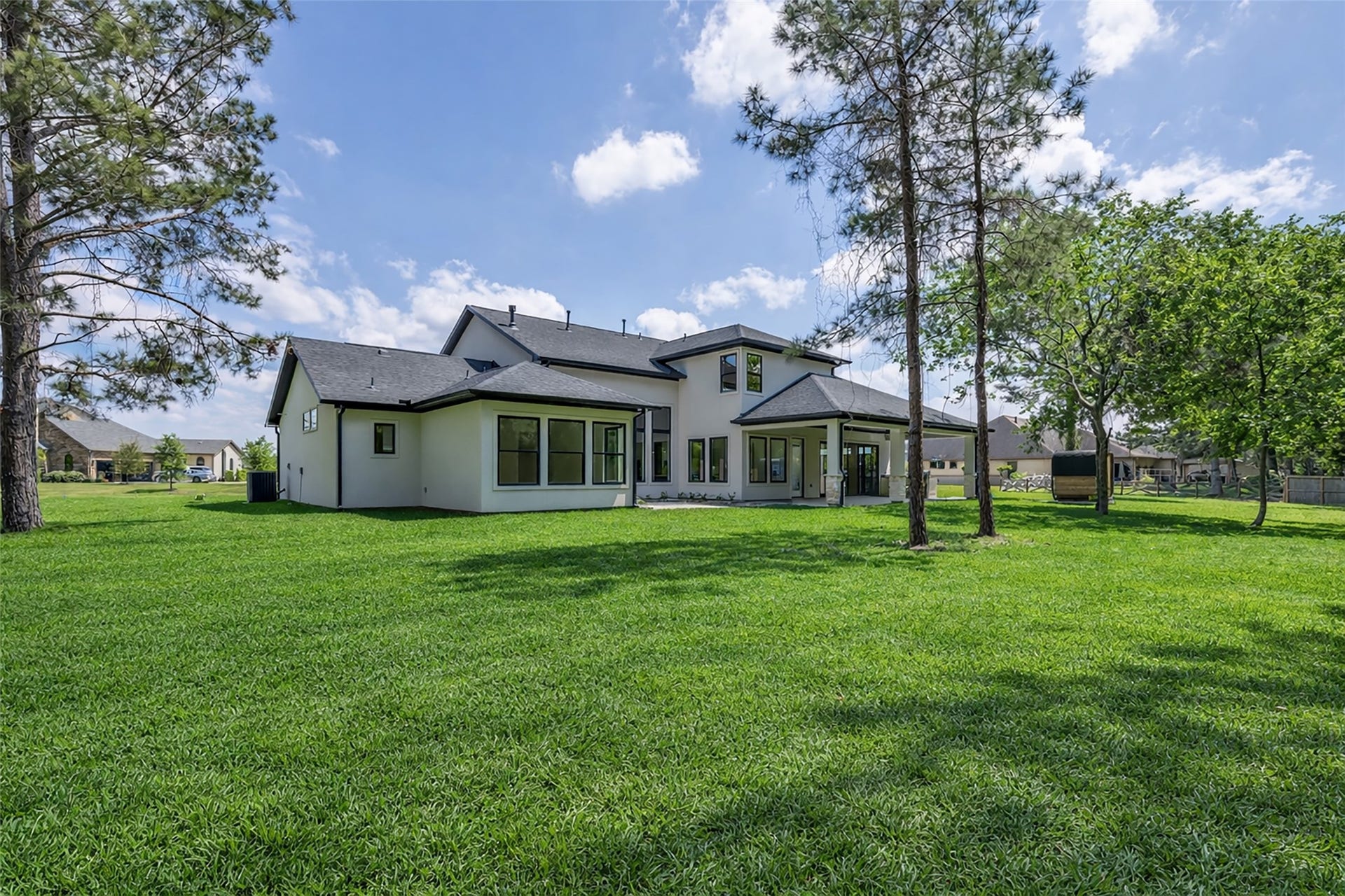 22420 Meadowhurst Circle W, Tomball, TX 77377 This photo showcases a modern home with large windows and a spacious backyard, surrounded by lush greenery and trees, providing a serene and private outdoor setting.