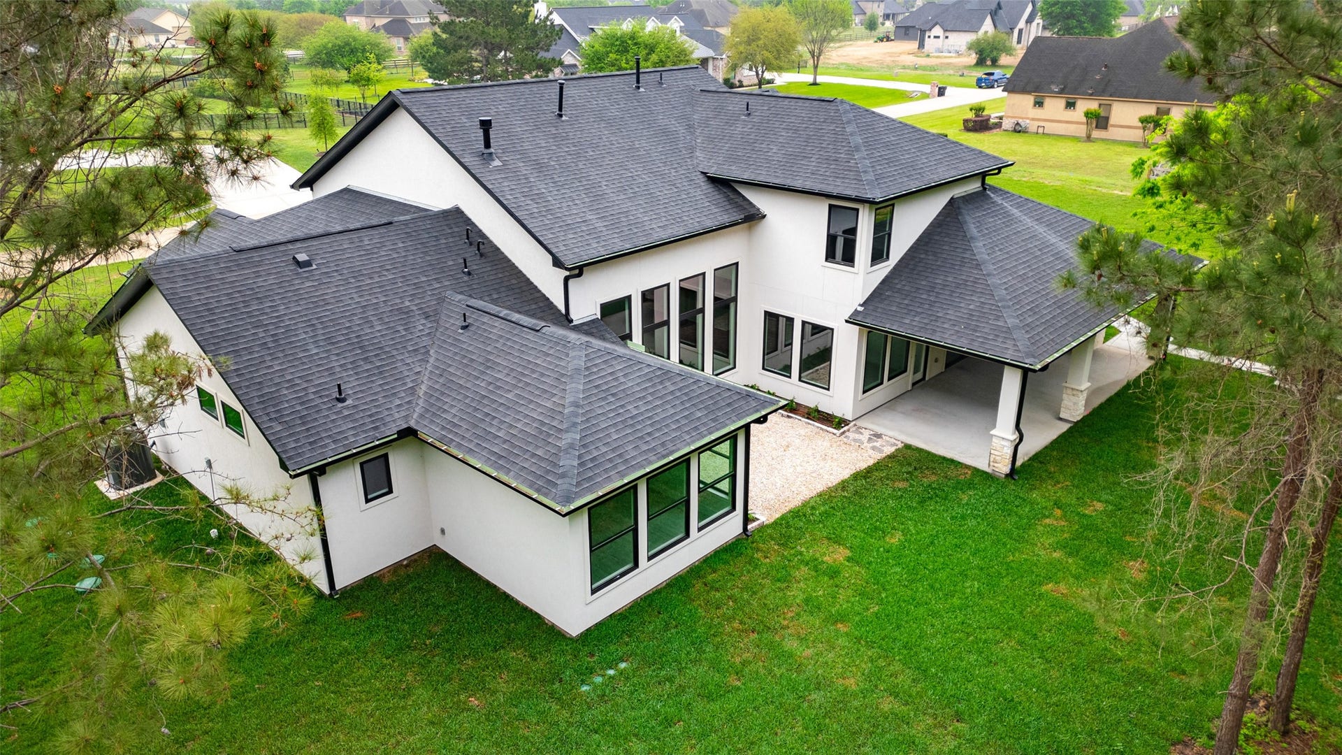 22420 Meadowhurst Circle W, Tomball, TX 77377 This aerial view showcases a modern two-story home with a dark roof, large windows, and a spacious backyard. It features a covered patio area and is surrounded by lush greenery, offering both privacy and a serene setting.