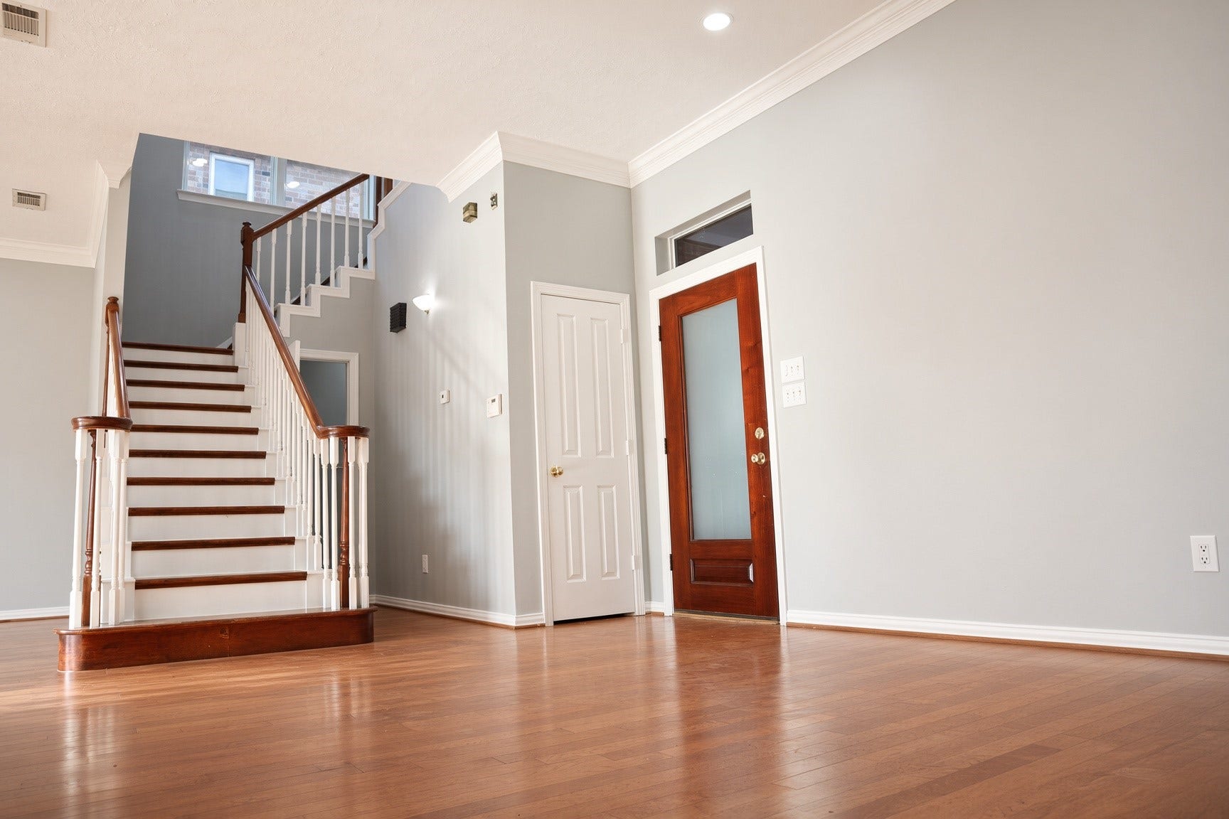 114 Oyster Creek Drive, Sugar Land, TX 77478 Elegant entryway with hardwood floors and a grand staircase, complemented by soft gray walls and a stylish wooden front door. With a half bath tucked away, in the corner.