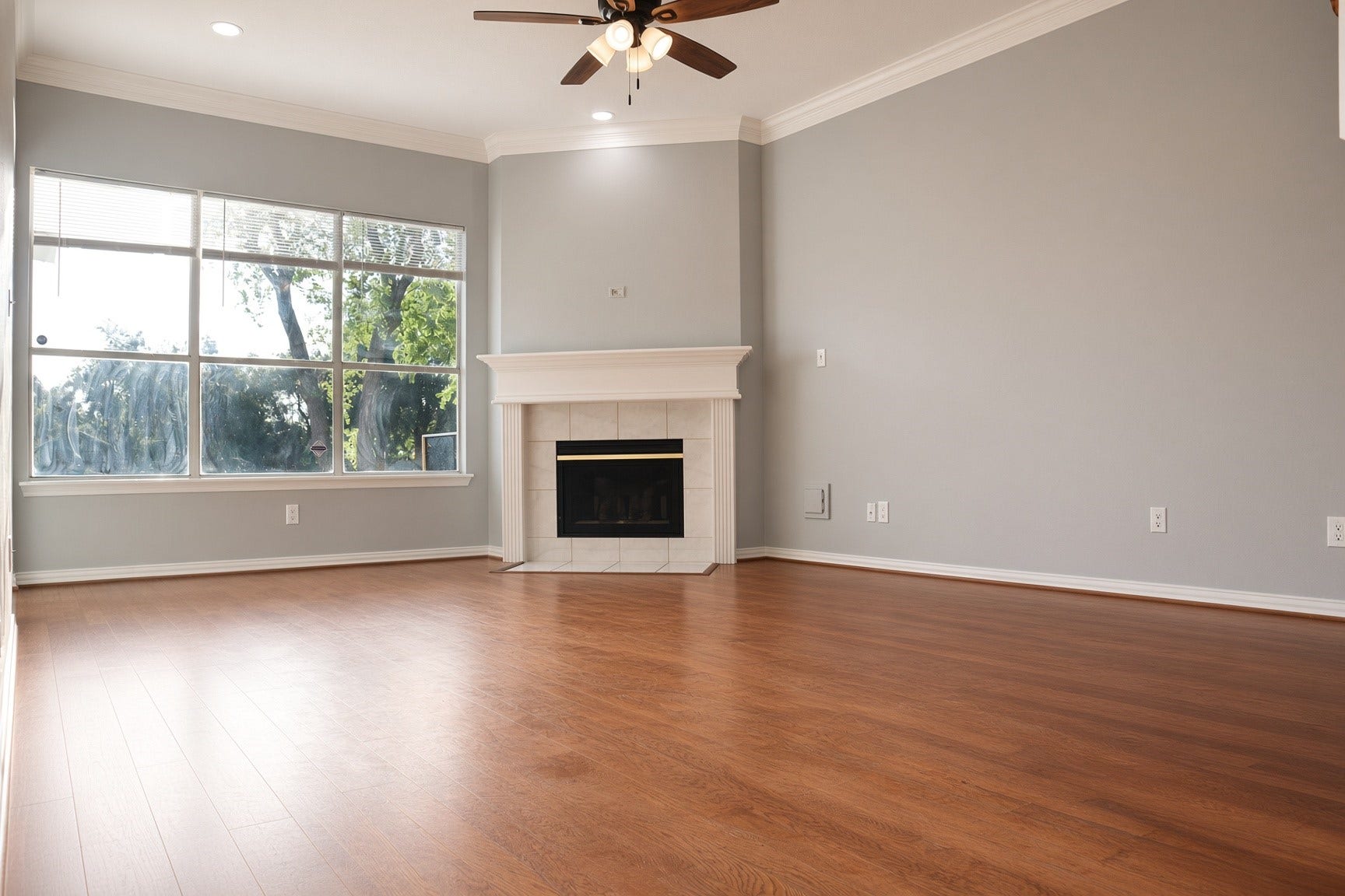 114 Oyster Creek Drive, Sugar Land, TX 77478 Spacious living room with elegant wood flooring, large windows for natural light, and a cozy fireplace, perfect for relaxation and gatherings.