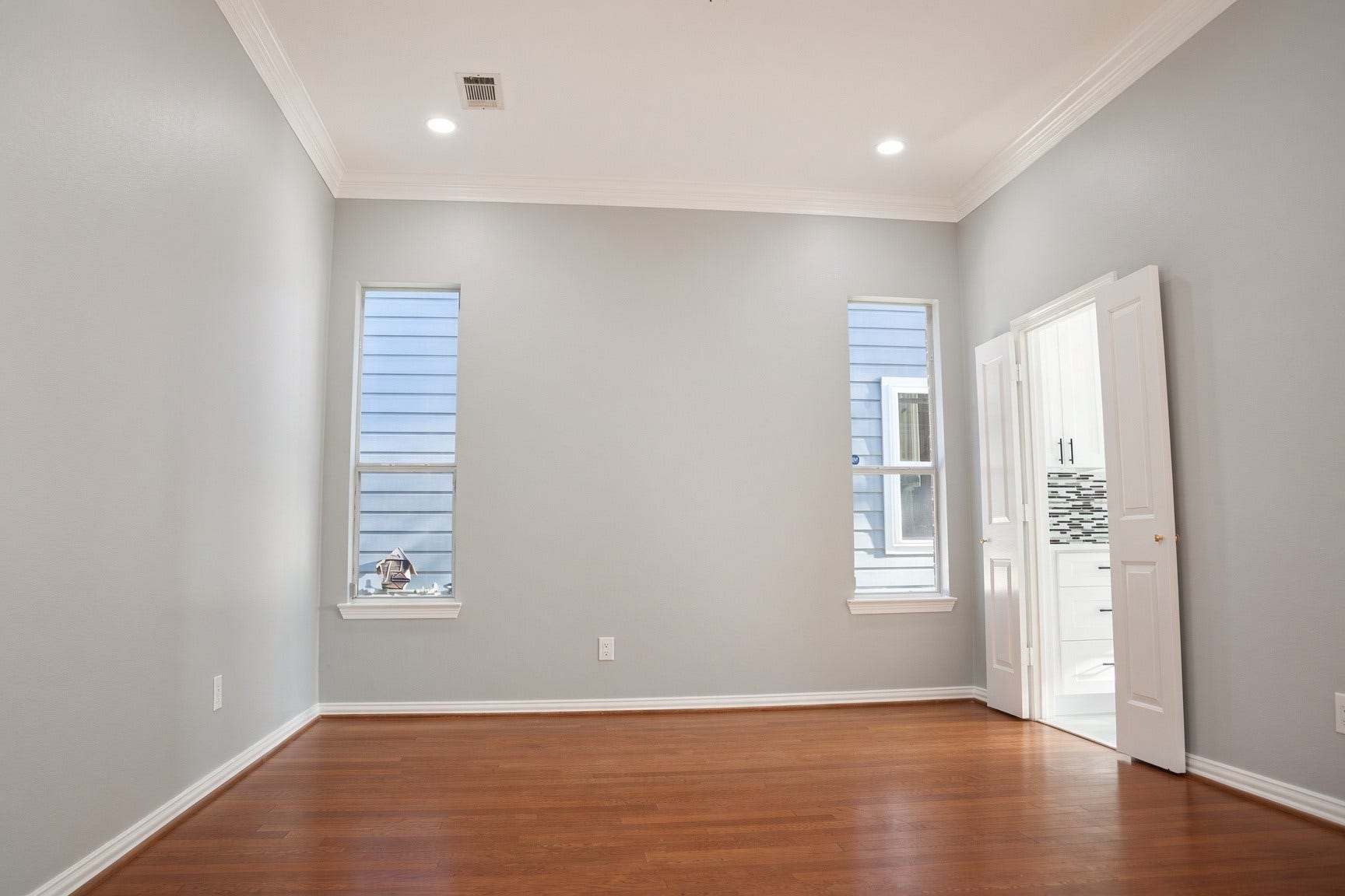 114 Oyster Creek Drive, Sugar Land, TX 77478 Bright room with hardwood floors, recessed lighting, and sleek gray walls, featuring tall windows for ample natural light.