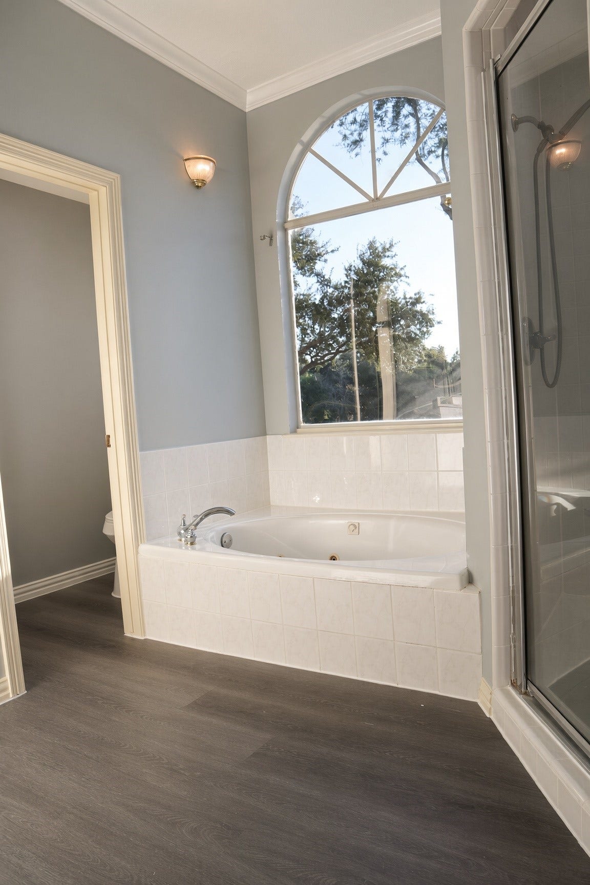 114 Oyster Creek Drive, Sugar Land, TX 77478 Elegant bathroom featuring a spacious soaking tub, large arched window with serene views, and a sleek glass-enclosed shower.