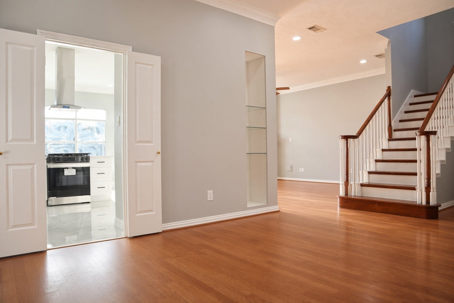 114 Oyster Creek Drive, Sugar Land, TX 77478 Spacious living area with elegant wood flooring, leading to a modern kitchen through double doors. A stylish staircase enhances the open layout.