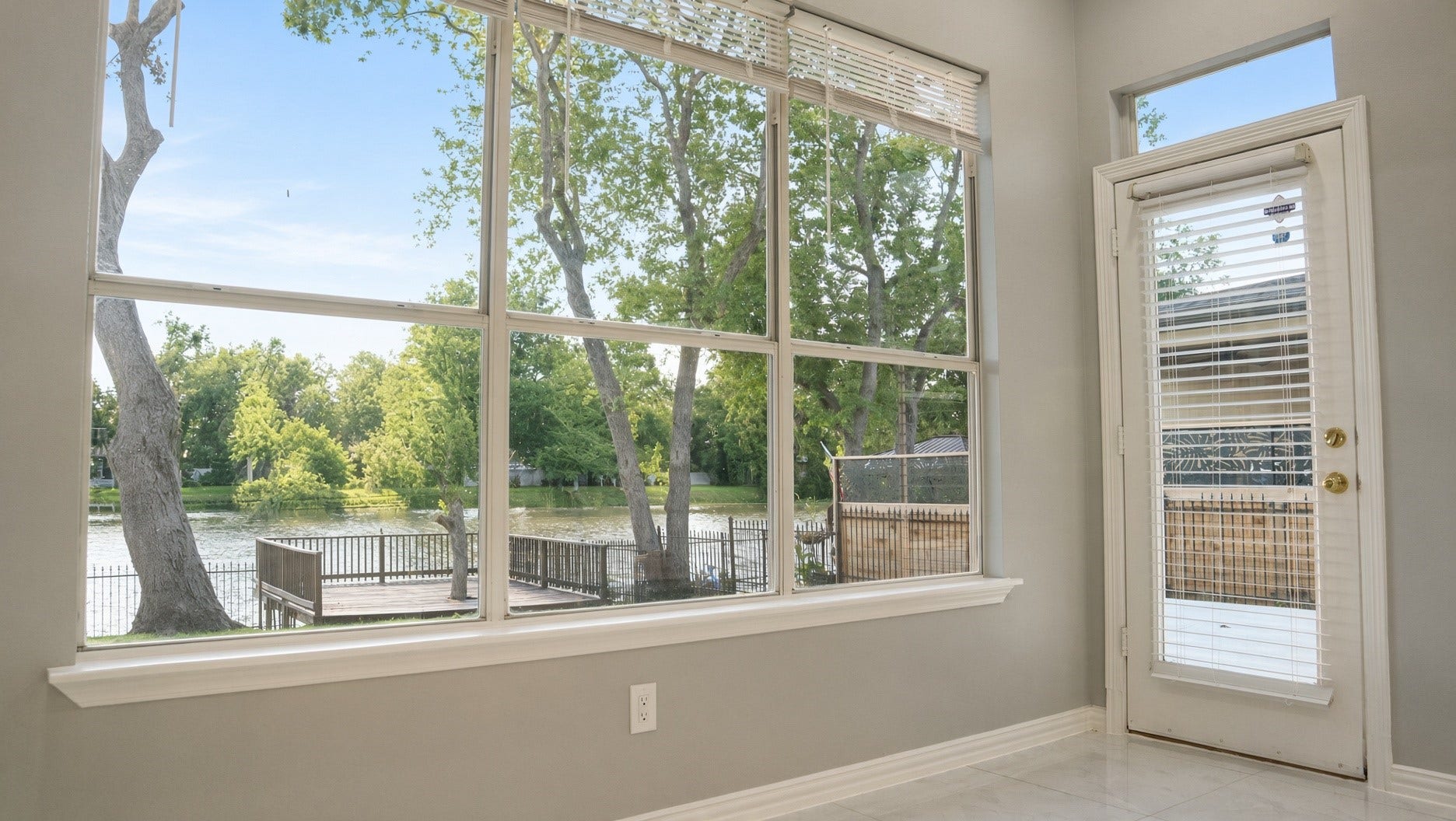 114 Oyster Creek Drive, Sugar Land, TX 77478 Bright room with large windows offering serene water views and a door leading to a private deck, perfect for relaxation and enjoying nature.