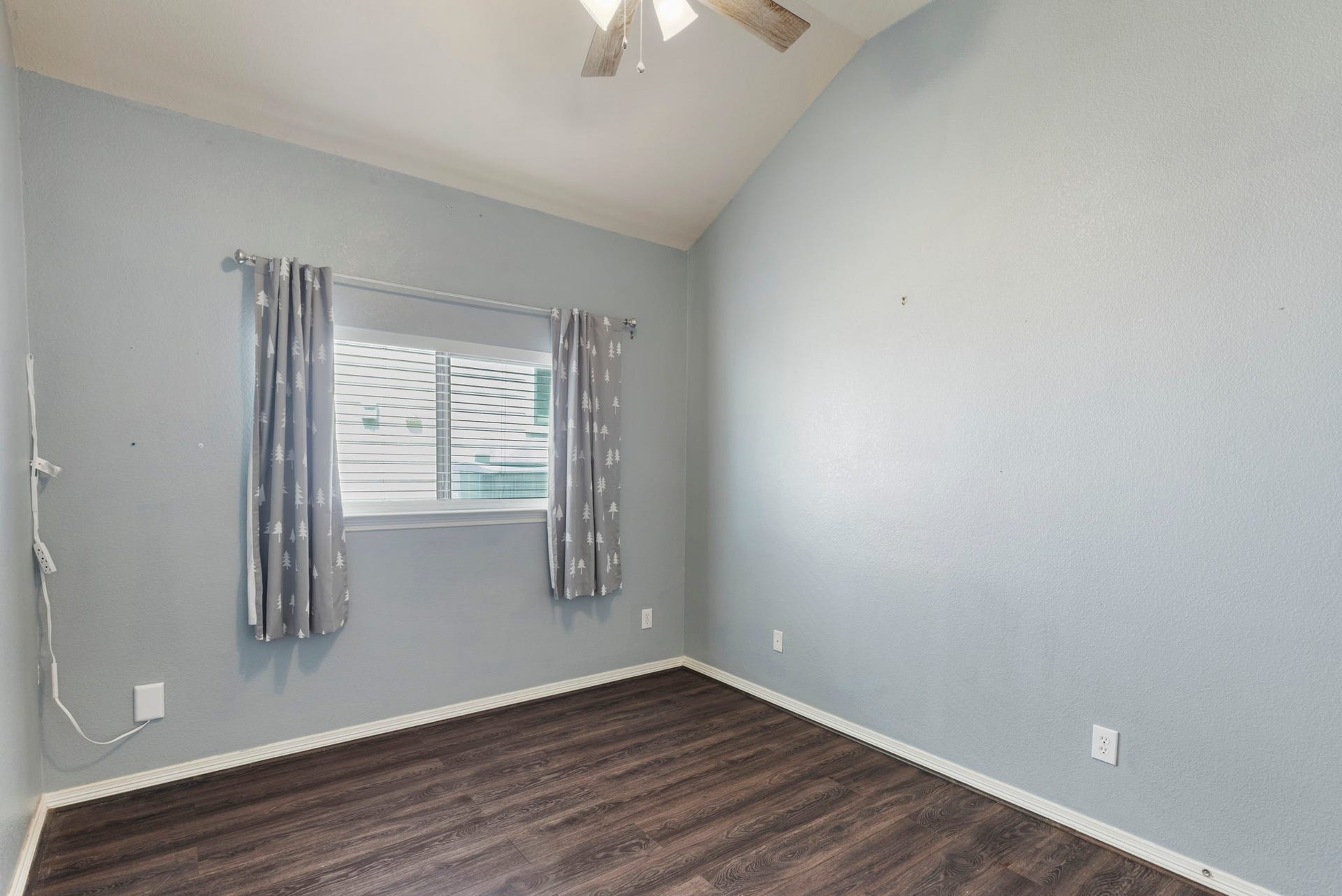 8022 N Tarrytown Crossing Drive, Conroe, TX 77304 A bright room featuring a vaulted ceiling, laminate flooring, and a large window with curtains, perfect for a cozy bedroom or office space.