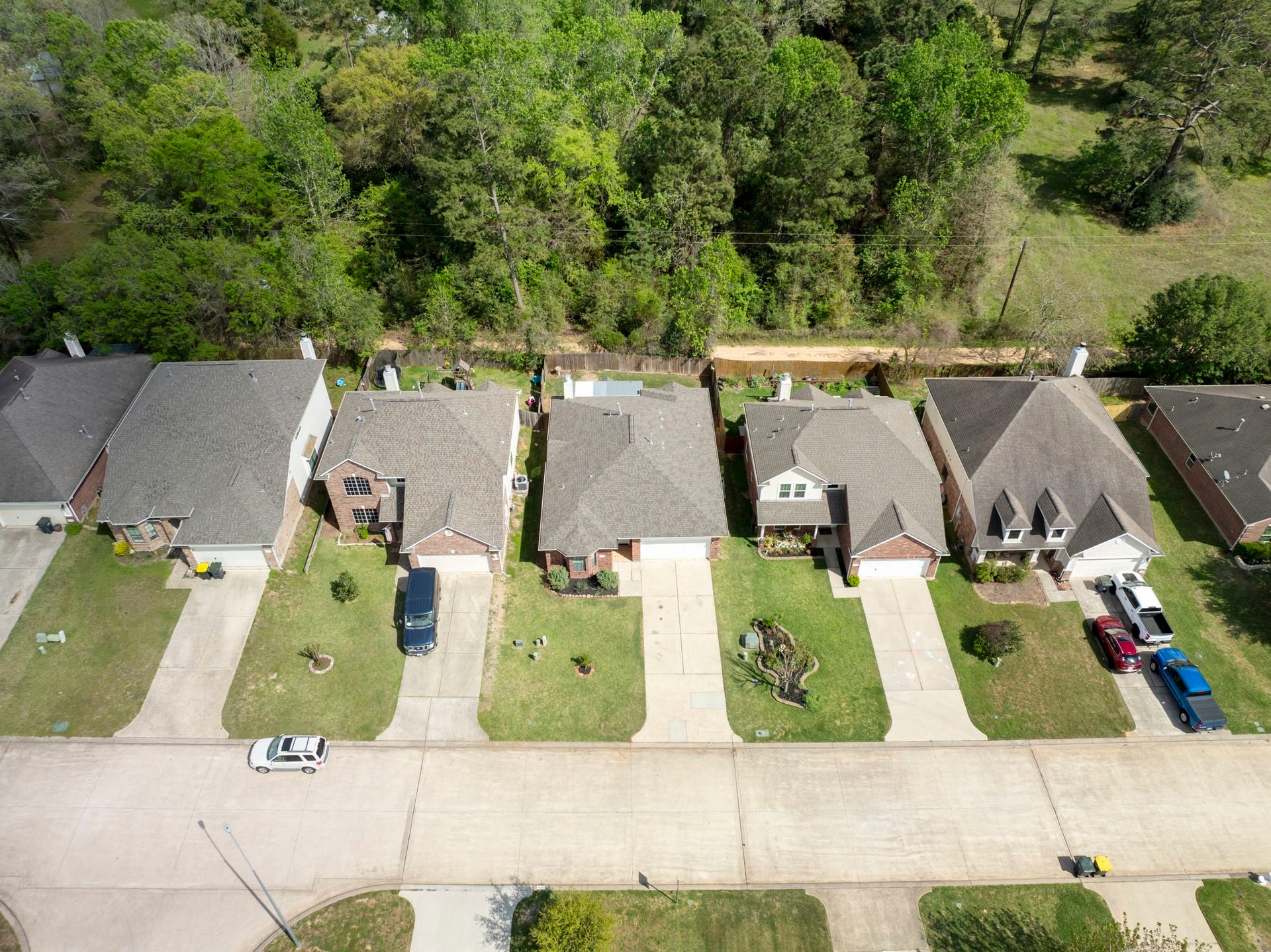 8022 N Tarrytown Crossing Drive, Conroe, TX 77304 Charming neighborhood featuring a row of well-maintained, single-family homes with spacious driveways. The lush greenery of the surrounding trees offers a serene, natural backdrop.