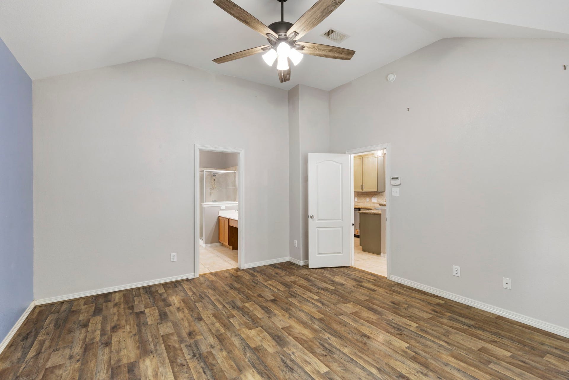 8022 N Tarrytown Crossing Drive, Conroe, TX 77304 Expansive primary bedroom featuring elegant laminateflooring, vaulted ceilings with a stylish fan, and direct access to a luxurious en-suite bathroom, creating a serene and sophisticated retreat.