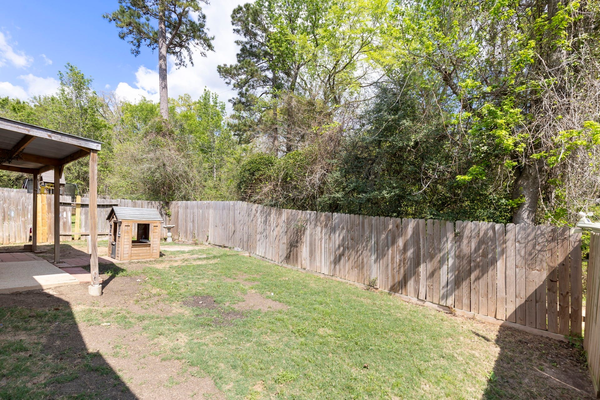8022 N Tarrytown Crossing Drive, Conroe, TX 77304 Charming backyard with a cozy covered patio and a quaint playhouse, bordered by lush greenery and a wooden fence, perfect for outdoor enjoyment.