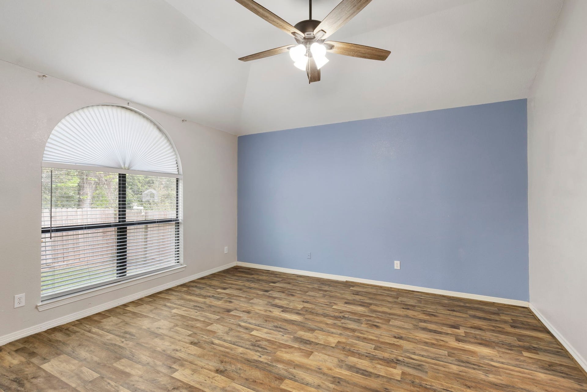 8022 N Tarrytown Crossing Drive, Conroe, TX 77304 Experience tranquility in this spacious primary bedroom featuring a soothing blue accent wall, elegant arched window, and rich laminate flooring, perfect for restful nights.