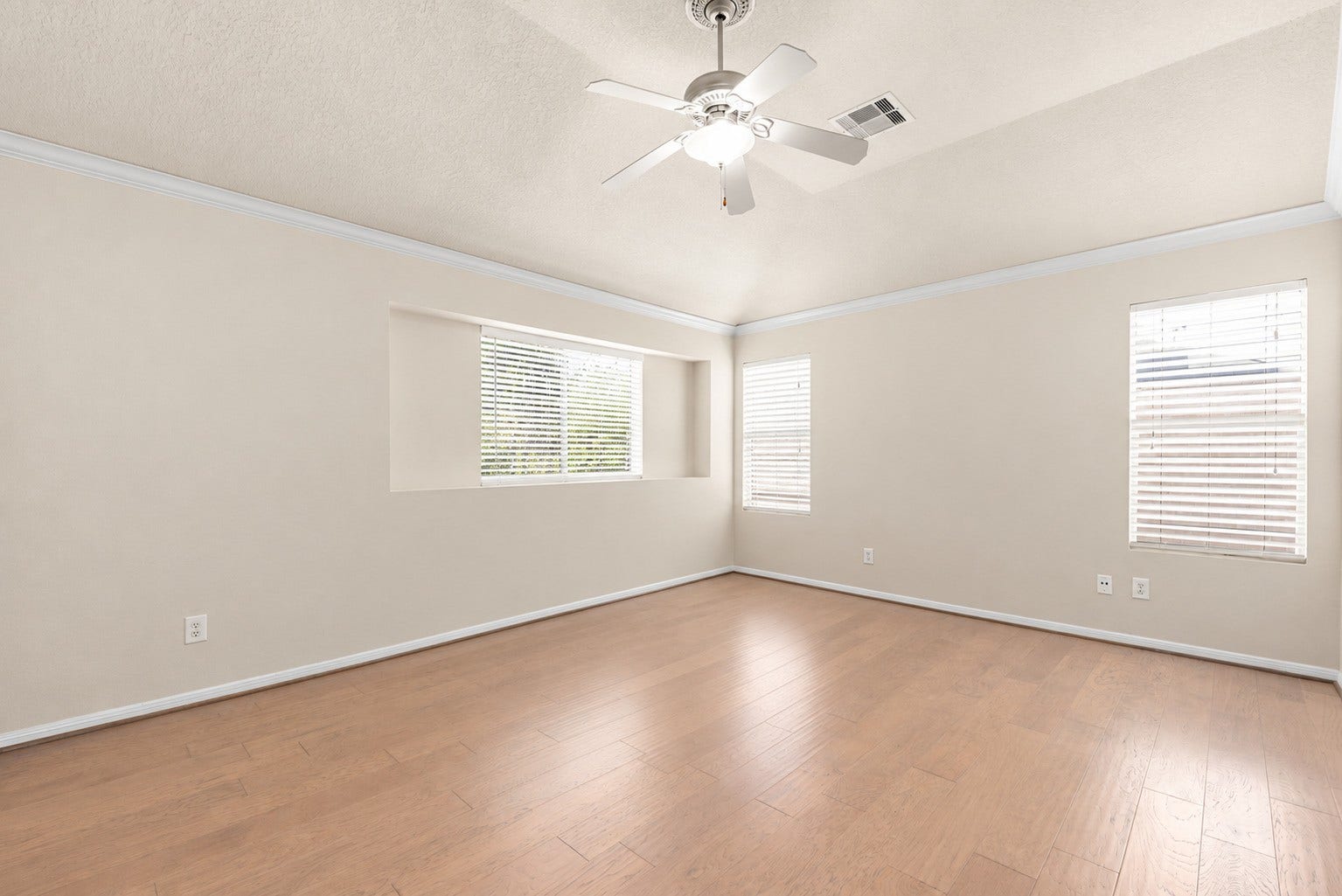 Second-floor primary bedroom with three windows that bring in natural light and wood-look flooring keeps the room bright and inviting.