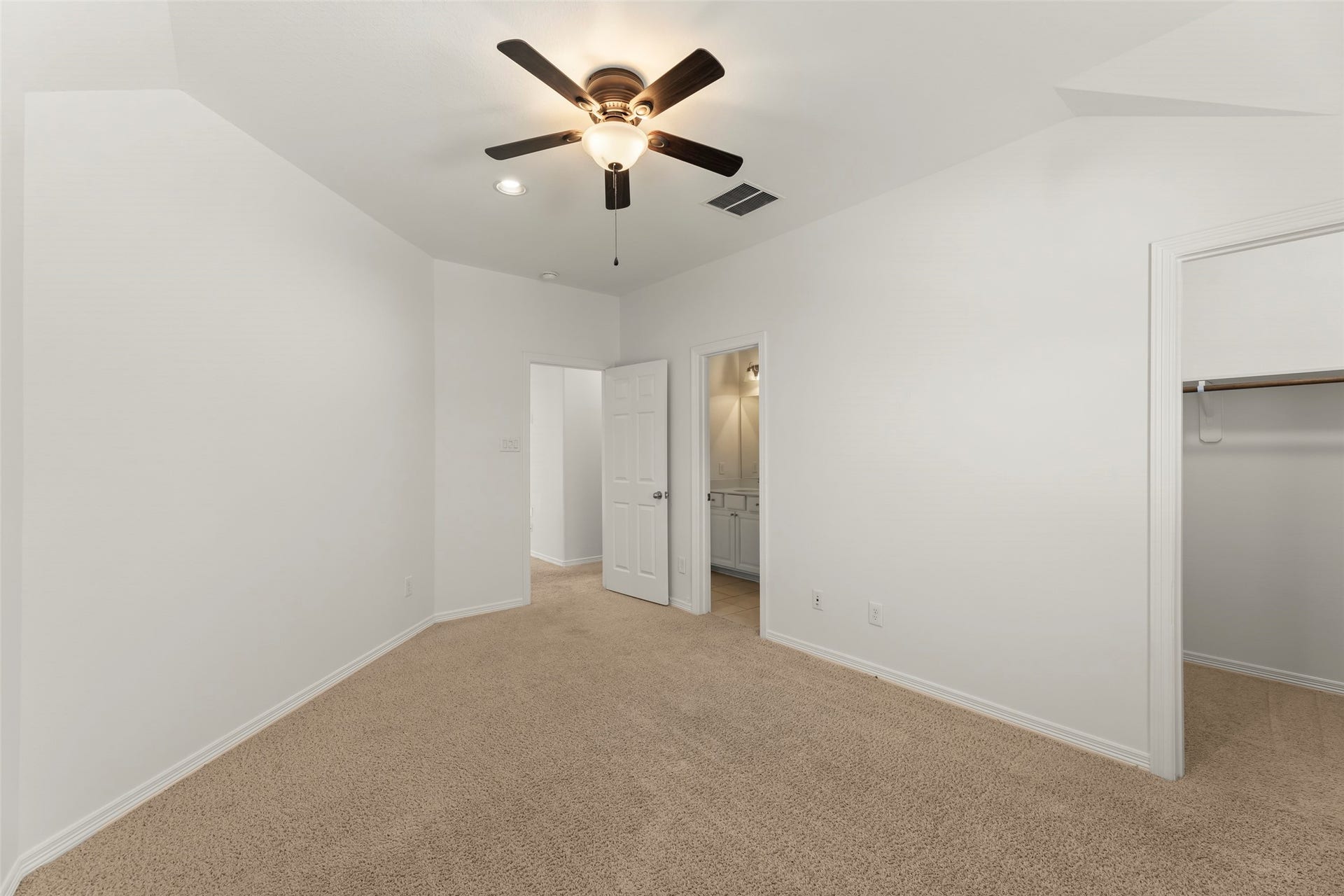 Large bedroom with plush carpeting, neutral walls, a ceiling fan, and an en suite bathroom for added convenience.