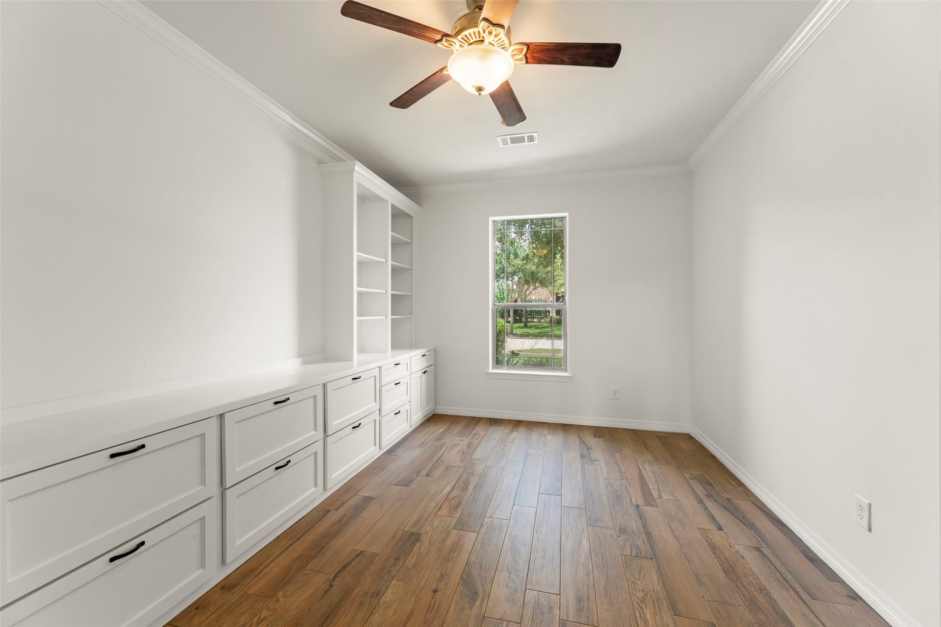 Built-in cabinetry, rich wood like flooring, and a ceiling fan, perfect for a home office or study.