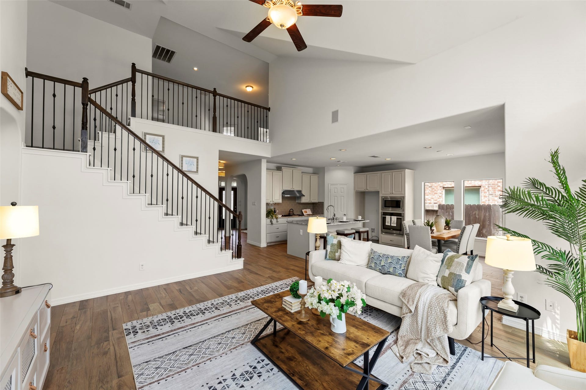 Inviting family room area with high ceilings, elegant staircase, and open-concept design flowing into a modern kitchen and dining space.
