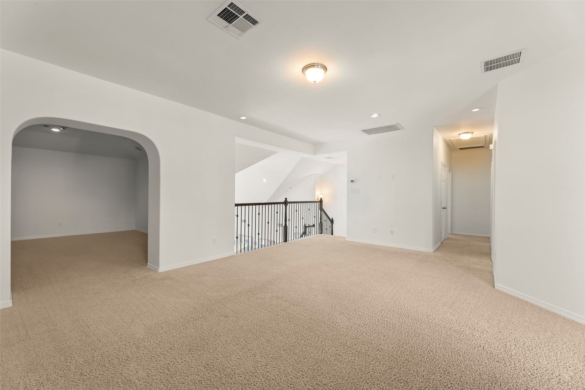 Upstairs area with plush carpet, featuring an arched entry leading to a cozy nook and an open view to the lower level, perfect for a versatile area.