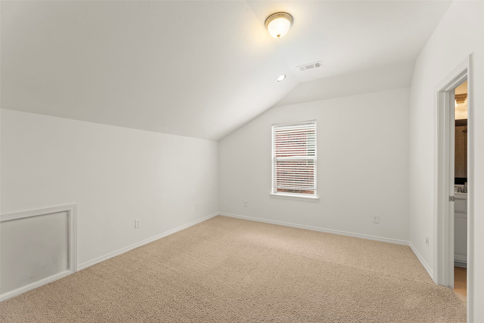 Comfortable bedroom with plush carpet, vaulted ceiling, and ample natural light from a large window.