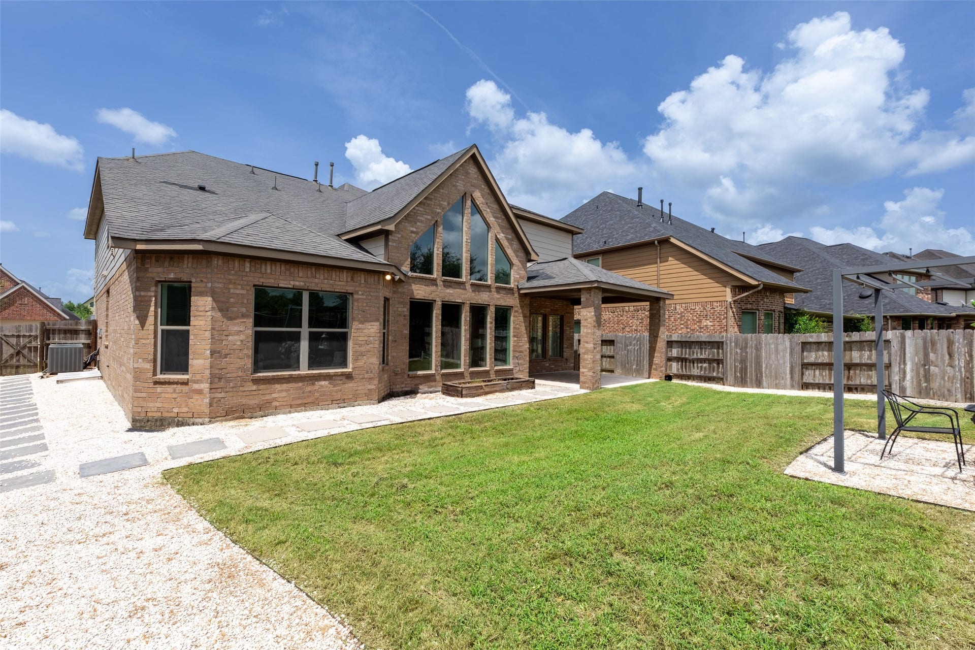 Stunning two-story brick home features expansive windows and a covered patio overlooking a spacious, well-maintained backyard, ideal for outdoor living and entertaining.