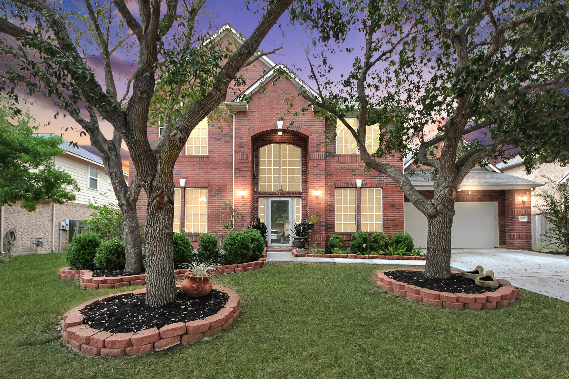 3003 Birch Landing Court, Pearland, TX 77584 A warm twilight glow settles over this beautiful brick home, casting soft highlights across the manicured lawn, raised garden beds, and mature trees that frame the entrance with quiet elegance.