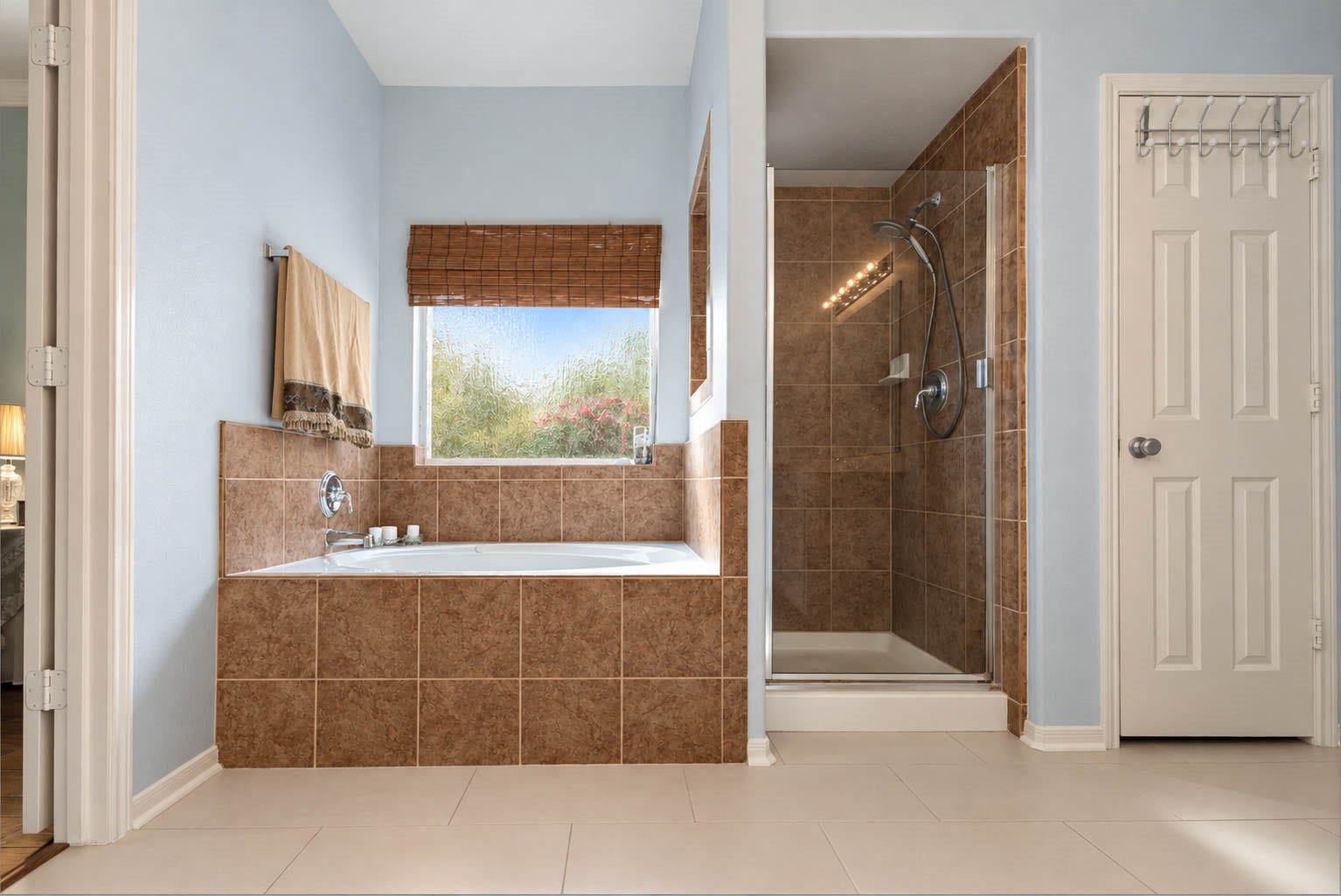 2532 Oak Dale Way, Seabrook, TX 77586 The primary bath feels like a spa, with a soaking tub framed by a warm tile surround and a rain glass window that brings in soft daylight while keeping things private. A separate walk in shower with a glass door and handheld showerhead sits beside it, and updated tile flooring ties the space together.