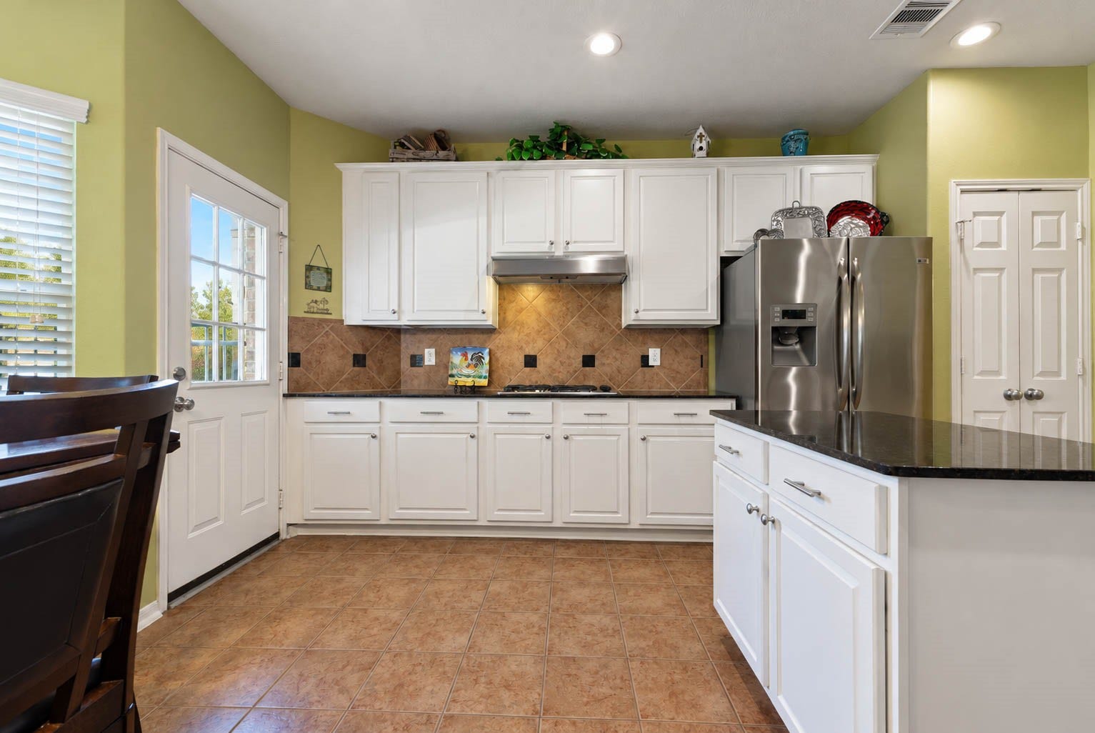 2532 Oak Dale Way, Seabrook, TX 77586 Another angle of the kitchen shows off a full wall of cabinetry with abundant storage, anchored by a gas cooktop beneath a sleek stainless hood. A diagonal tile backsplash adds warmth and texture, and a double door pantry keeps groceries and small appliances neatly tucked away.