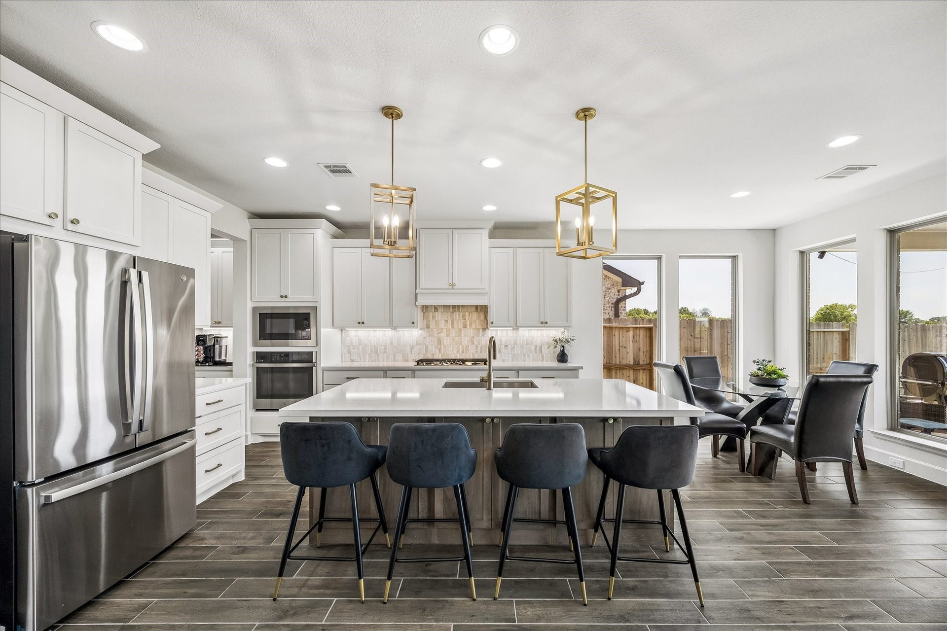 Chef's kitchen featuring a large quartz island, stainless steel appliances, custom cabinetry and designer pendant lighting