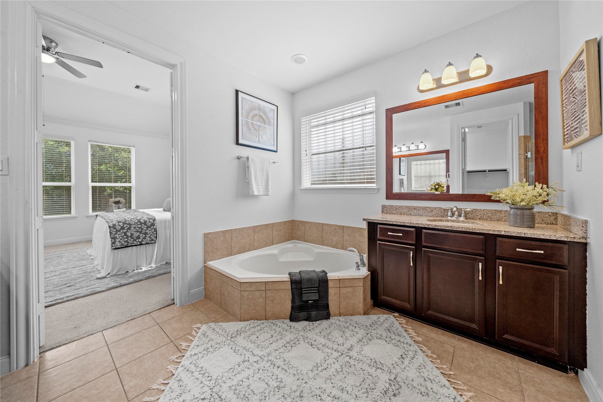 17315 Tomintoul Path, Richmond, TX 77407 A tranquil bath retreat highlights a corner soaking tub, granite-topped vanity, rich wood finishes, and natural light with convenient access to the primary suite.