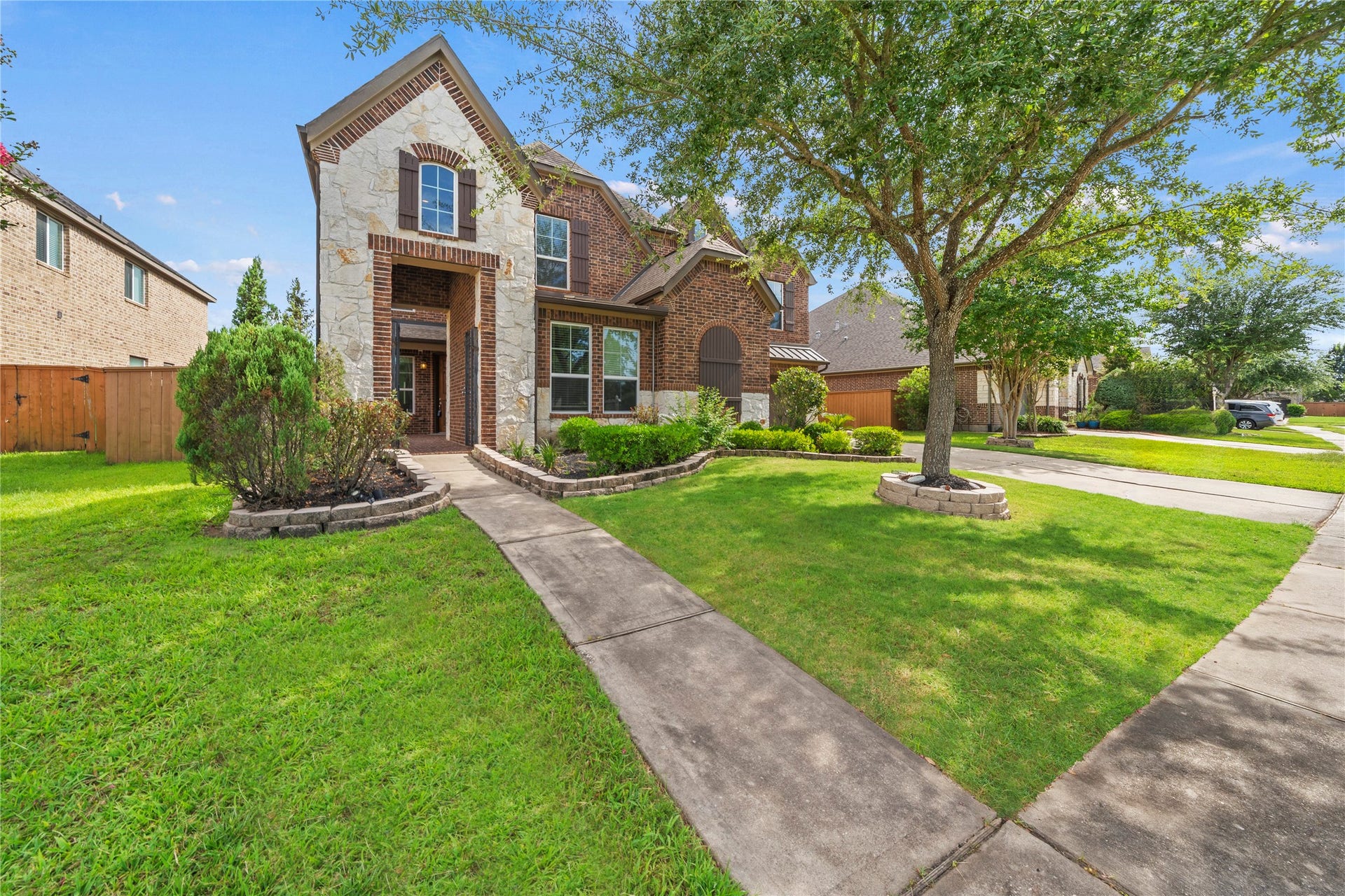 17315 Tomintoul Path, Richmond, TX 77407 An impressive two-story residence showcasing timeless brick and stone architecture, manicured landscaping, and a stately tree-lined setting that creates exceptional curb appeal.
