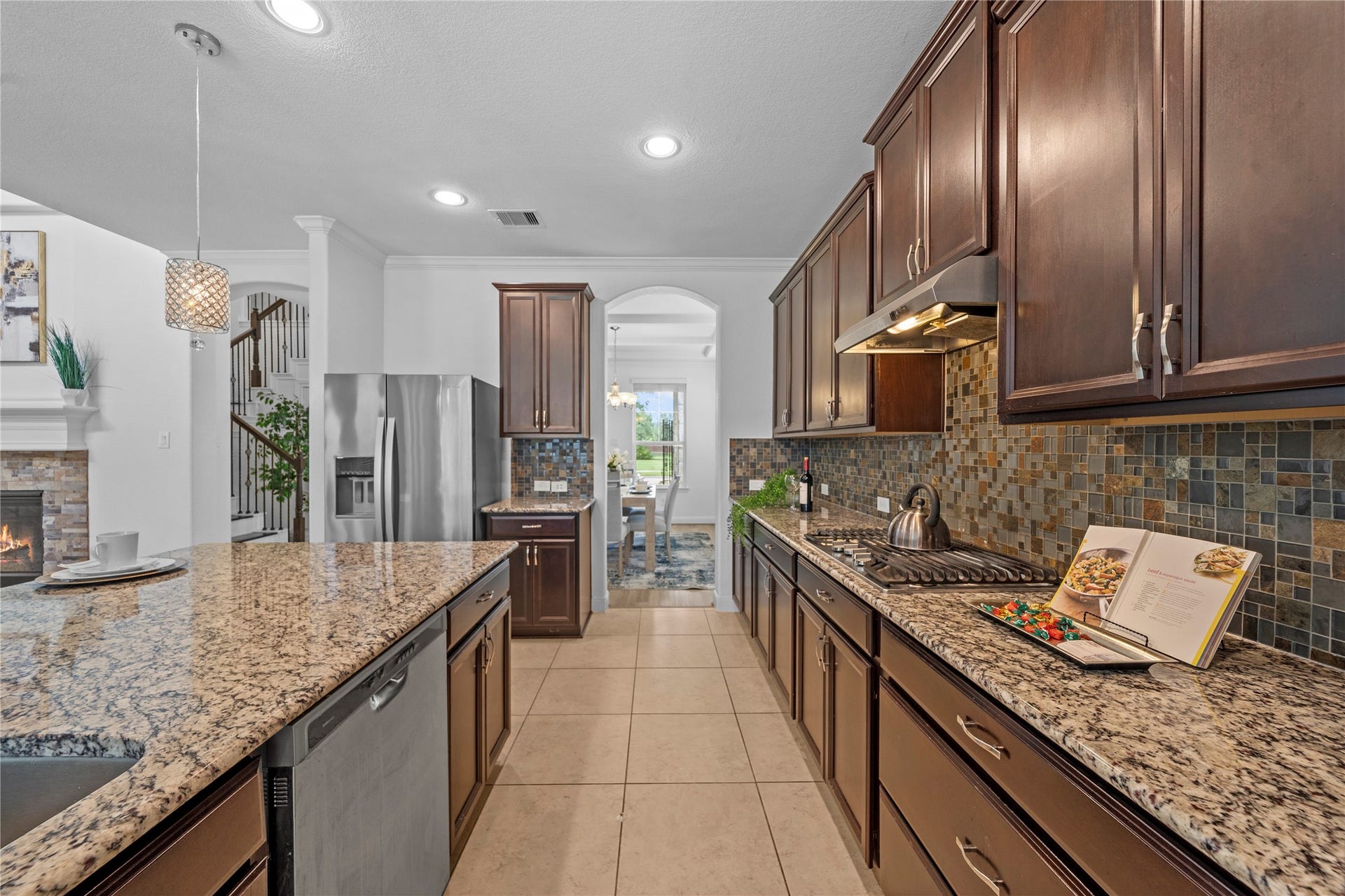17315 Tomintoul Path, Richmond, TX 77407 A refined culinary workspace features abundant custom cabinetry, polished granite countertops, a gas cooktop, and richly textured tilework for an elevated cooking experience.