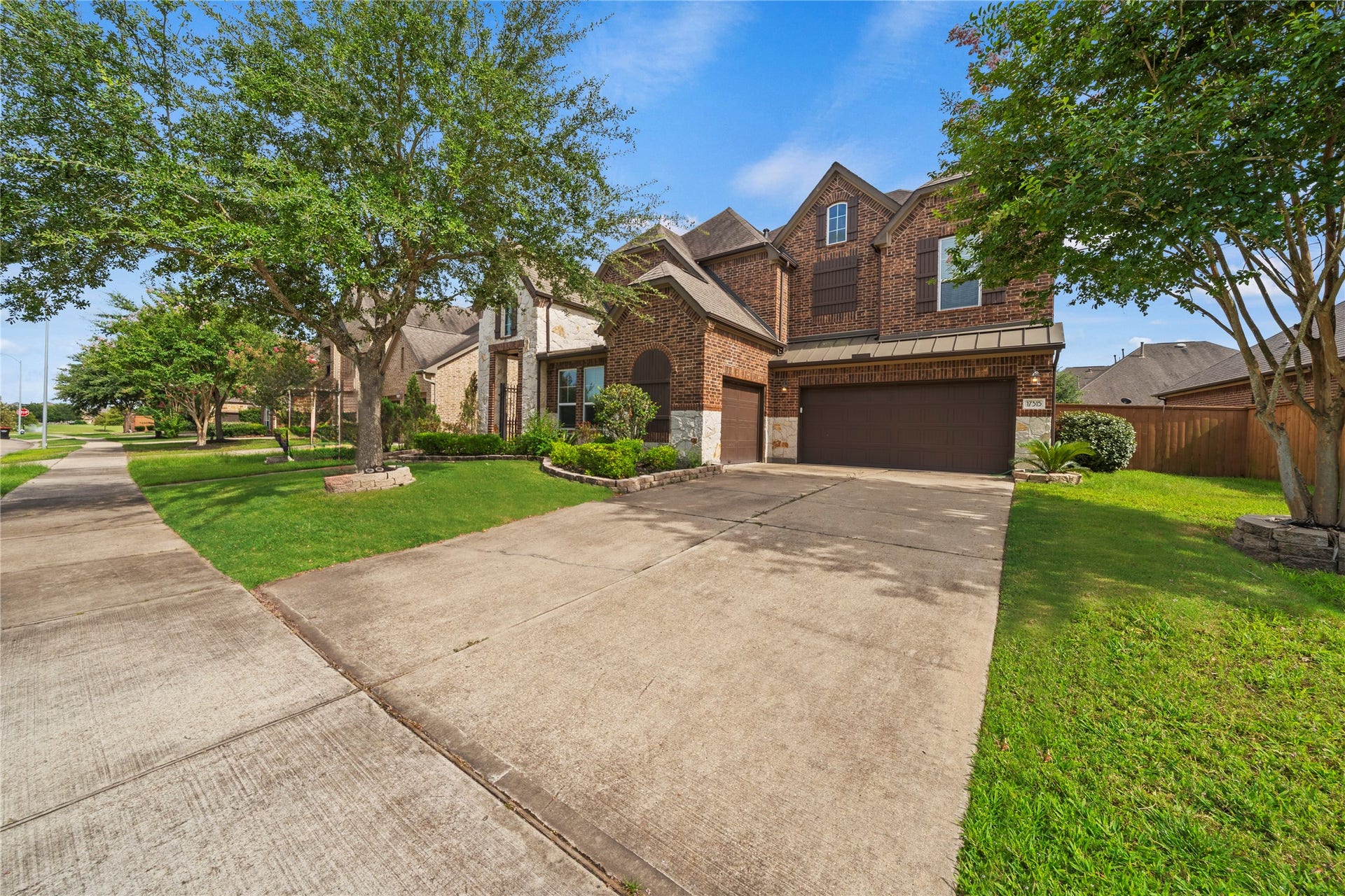 17315 Tomintoul Path, Richmond, TX 77407 A commanding driveway approach highlights the three-car garage, rich brick faade, and mature greenery, presenting a polished arrival with distinguished residential elegance.