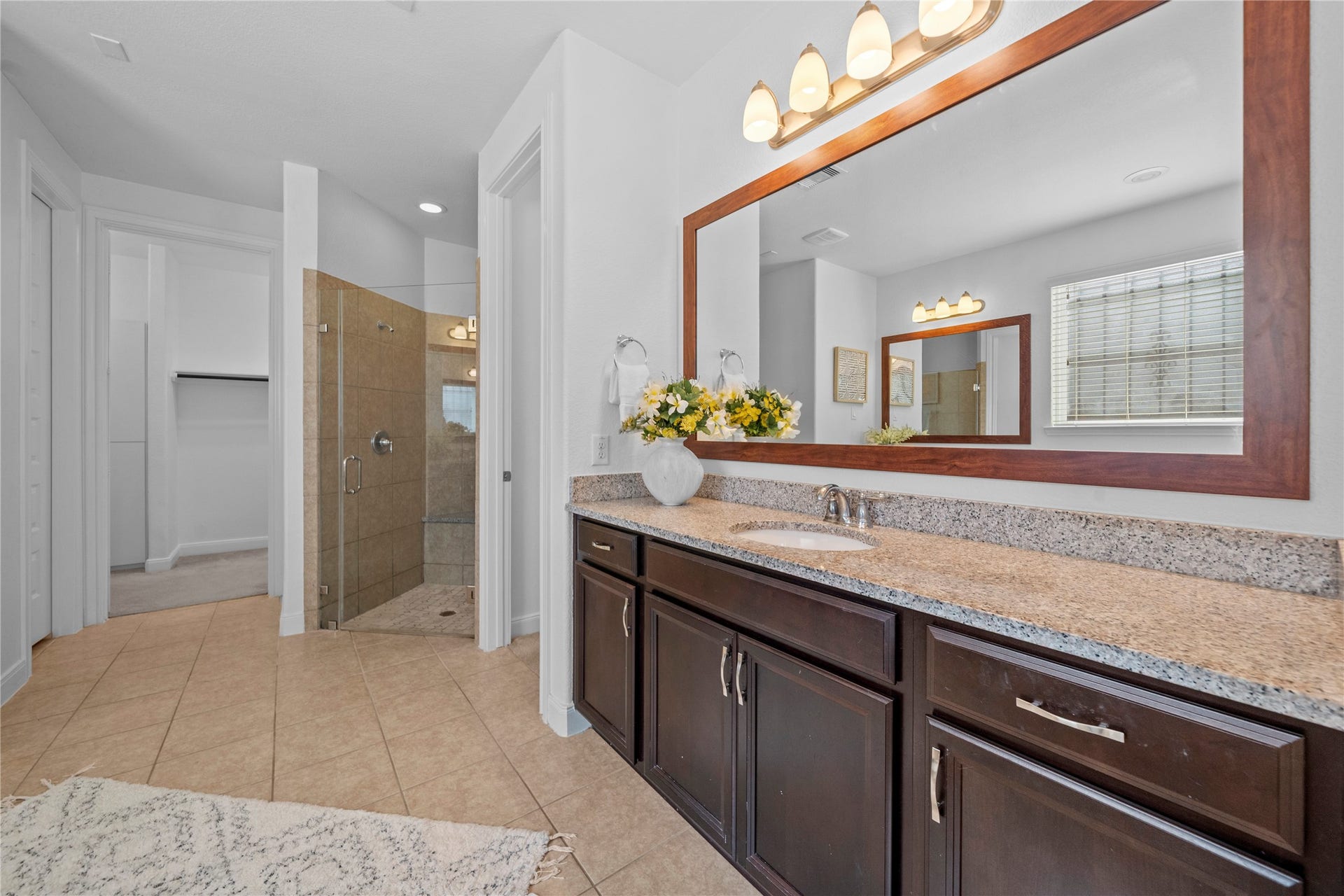 17315 Tomintoul Path, Richmond, TX 77407 A spa-inspired primary bath showcases an extended granite vanity, expansive framed mirror, warm wood cabinetry, and a glass-enclosed walk-in shower for everyday indulgence.