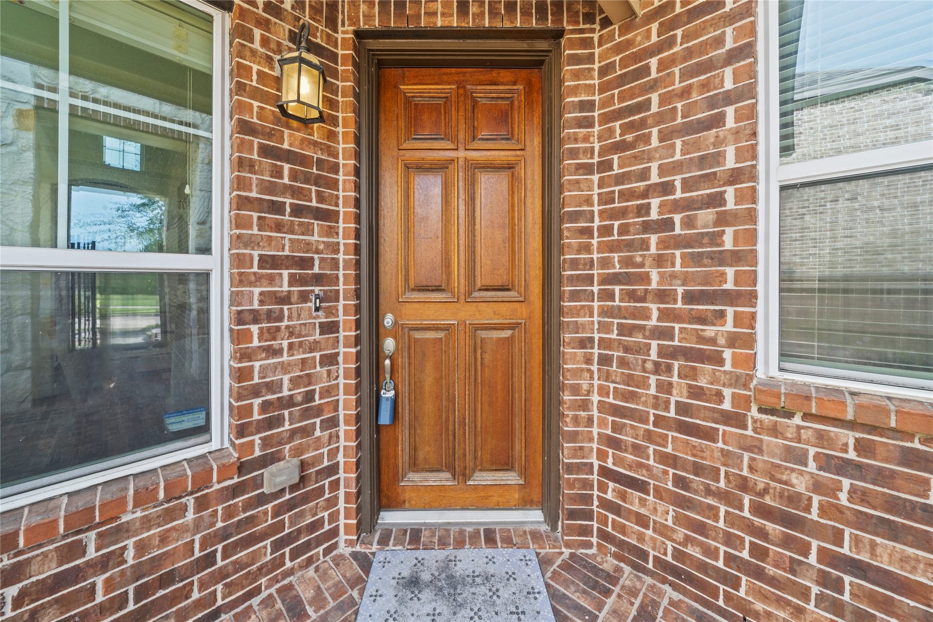 17315 Tomintoul Path, Richmond, TX 77407 A handsome paneled wood entry door framed by classic brickwork and warm lantern lighting creates a welcoming introduction to the residence.