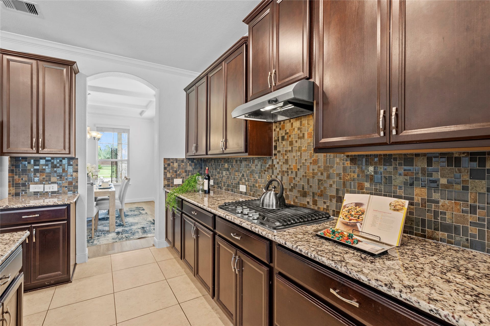 17315 Tomintoul Path, Richmond, TX 77407 Rich cabinetry, gleaming granite surfaces, and a mosaic tile backsplash frame the gas cooktop, creating a polished setting for inspired culinary pursuits.