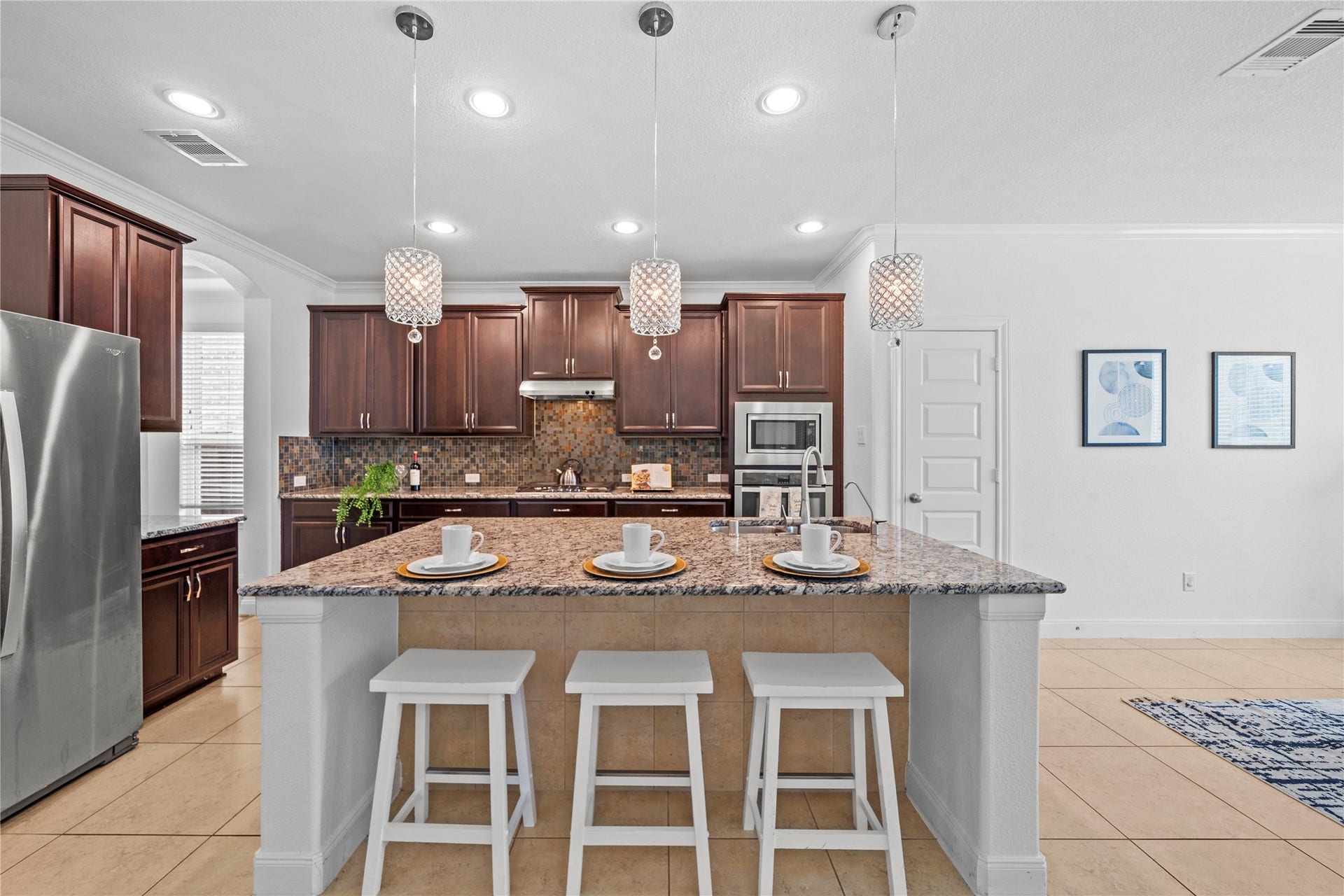 17315 Tomintoul Path, Richmond, TX 77407 A chef-inspired kitchen showcases rich wood cabinetry, expansive granite surfaces, stainless steel appliances, and sparkling pendant fixtures above the generous breakfast bar.