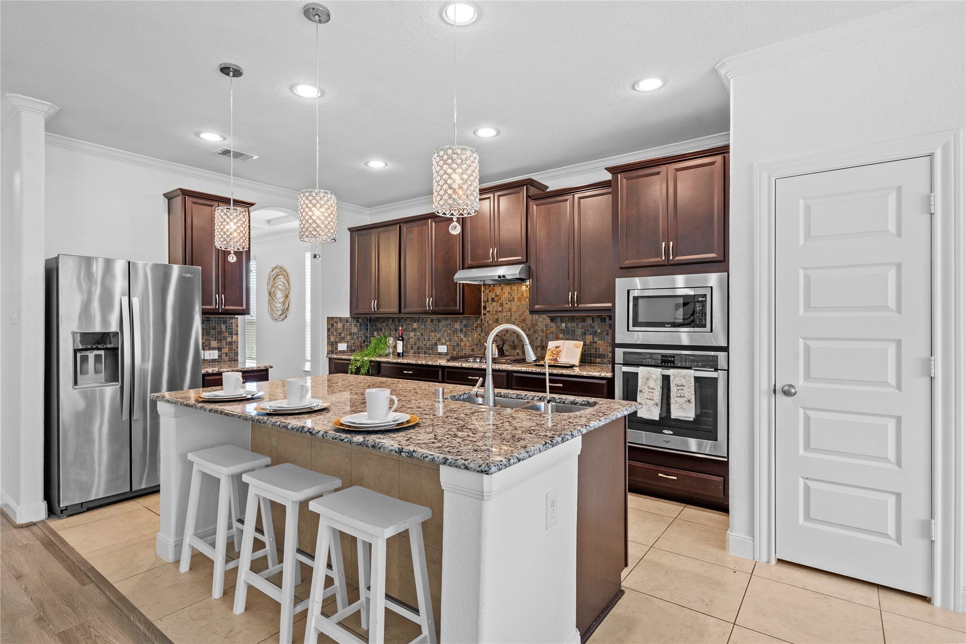 17315 Tomintoul Path, Richmond, TX 77407 At the heart of the home, this beautifully equipped kitchen presents an oversized granite island, mosaic backsplash, integrated stainless appliances, and luminous designer pendants.